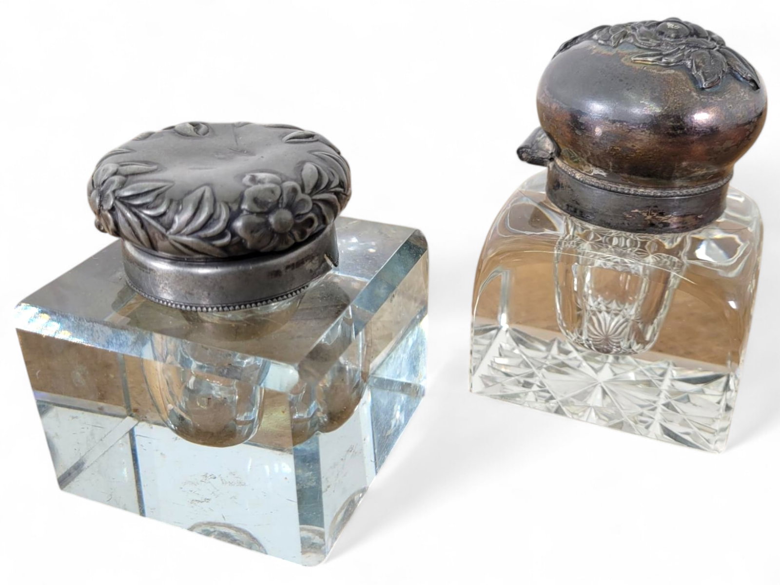 Pair of Antique Cut Glass Inkwells: A set of two square glass inkwells with intricately embossed silver-tone lids. The lids feature floral and vine patterns, complementing the clean, faceted bases. In good vintage condition. See photos 