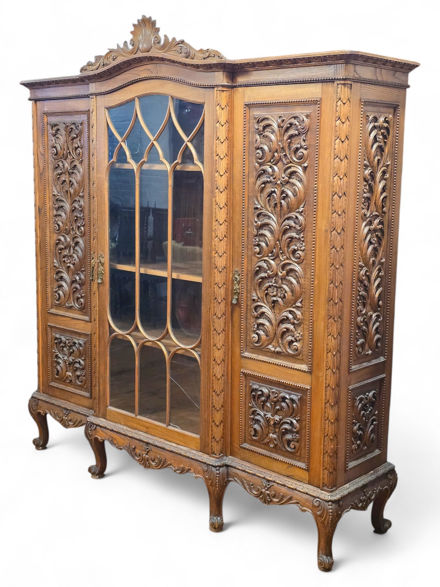 French Renaissance Style Carved Oak Display Cabinet:  Oak display/china cabinet with ornate carved wood decorations. Shell and foliate scroll crest and a central glass door with mullioned wood decorations. Notable cracks to two of the glass panels