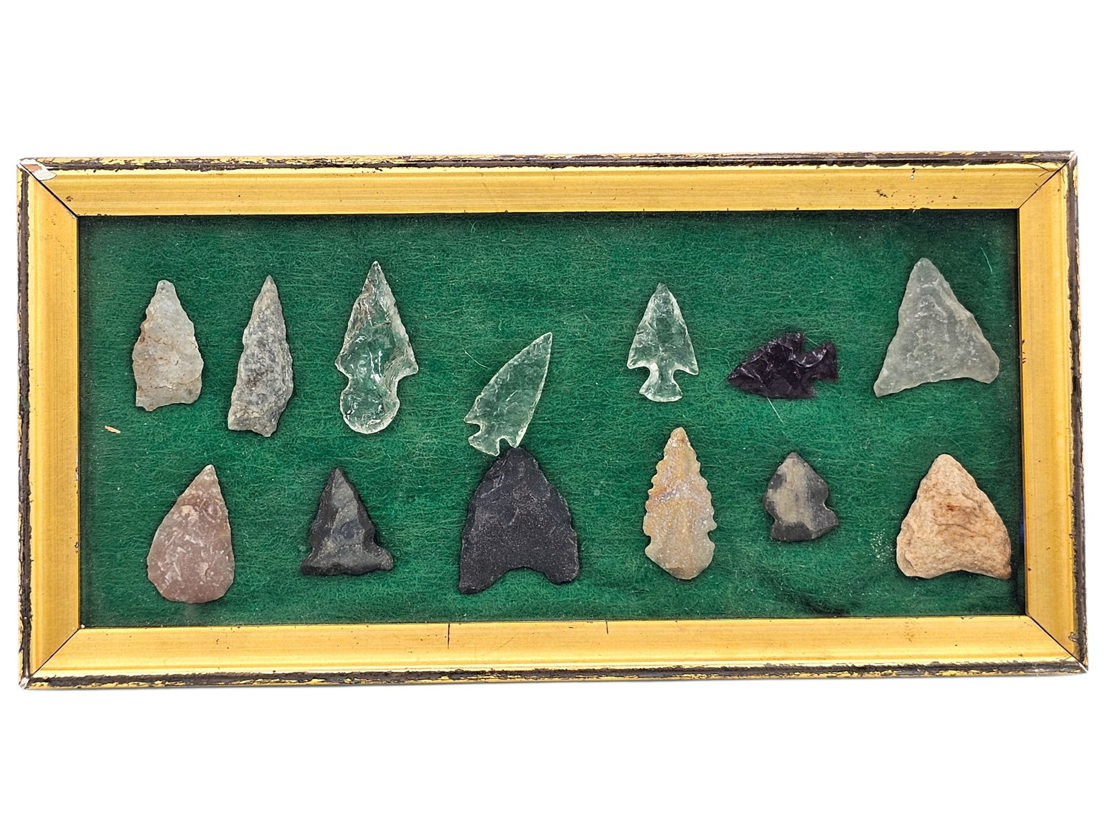 Grouping of Crystal & Stone Arrowheads- Clear & Translucent Red: Grouping of Native American crystal and stone arrowheads framed under glass. Notable arrowheads include 2 clear translucent arrowheads, likely agate, and a deep red translucent arrowhead, likely red o