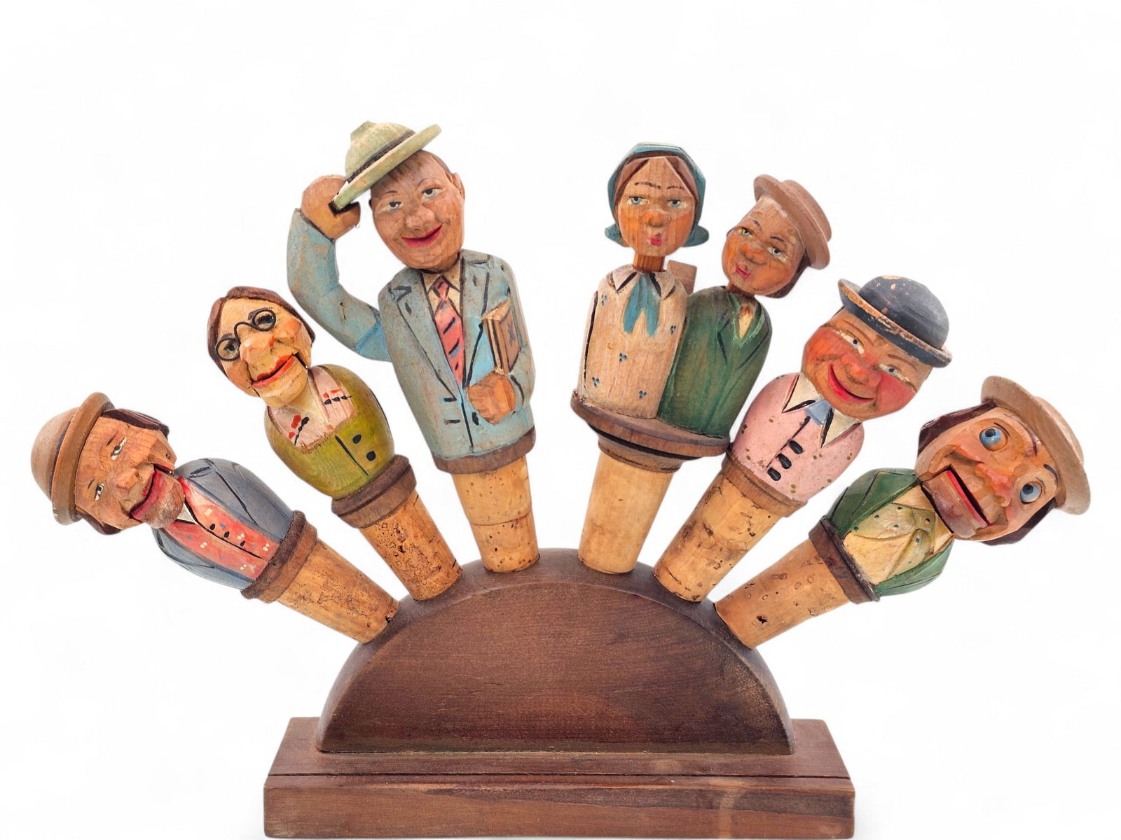 Grouping of 6 German Hand Carved Wood Mechanical Bottle Stoppers and Holder: This lot includes 6 wood hand carved and painted German bottle with corn ends along with a wooden stand. Many of the stoppers are mechanical, having tabs at the back that can be pressed to make figure