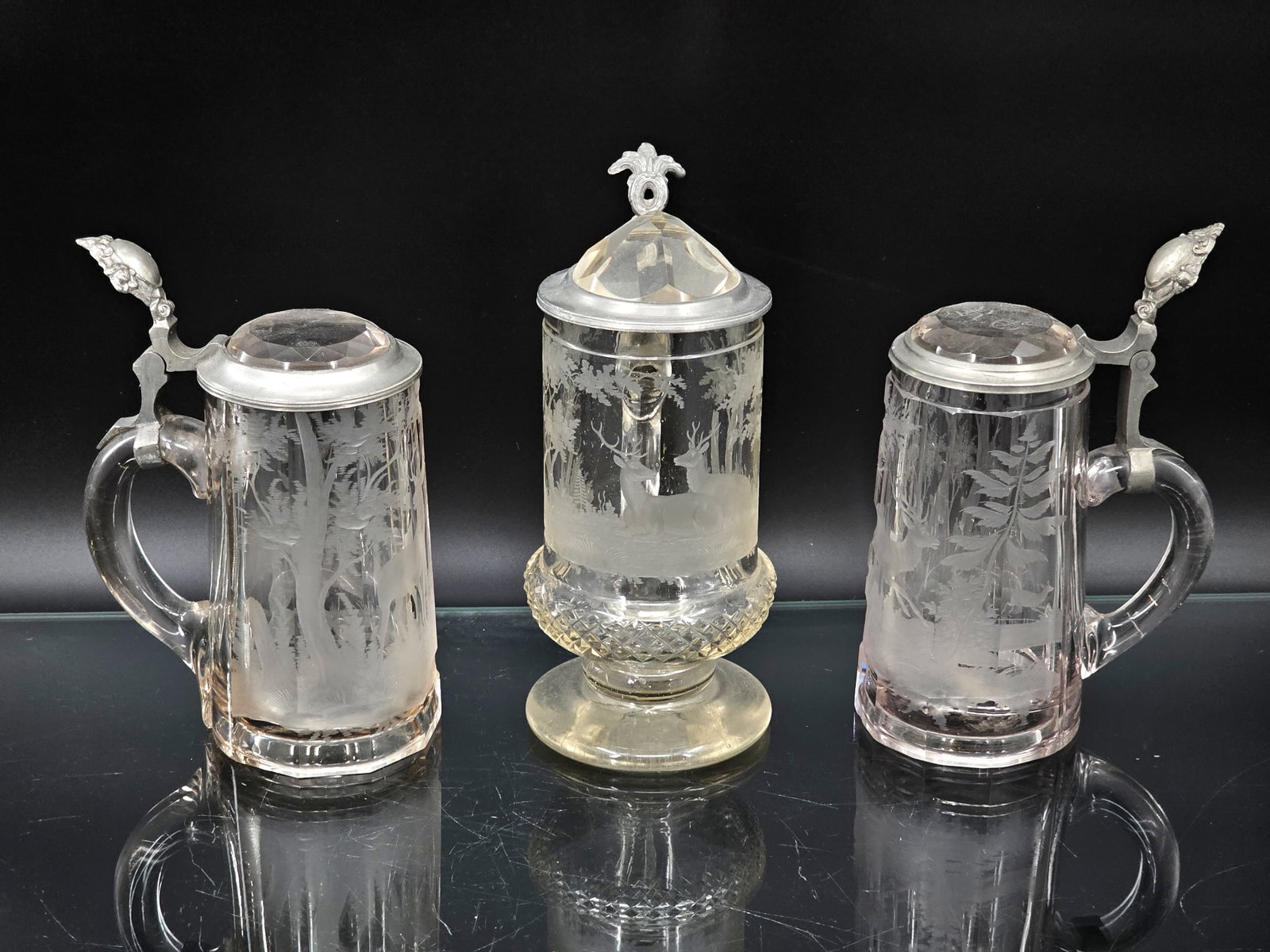 Grouping of 3 Vintage Etched Glass Beer Steins w/ Deer/Forest Scenes: Three German beer steins with acid etched forest stag and deer motifs on clear glass. Pewter accents and some cut glass details. Wear consistent with age and use including surface wear and oxidation.