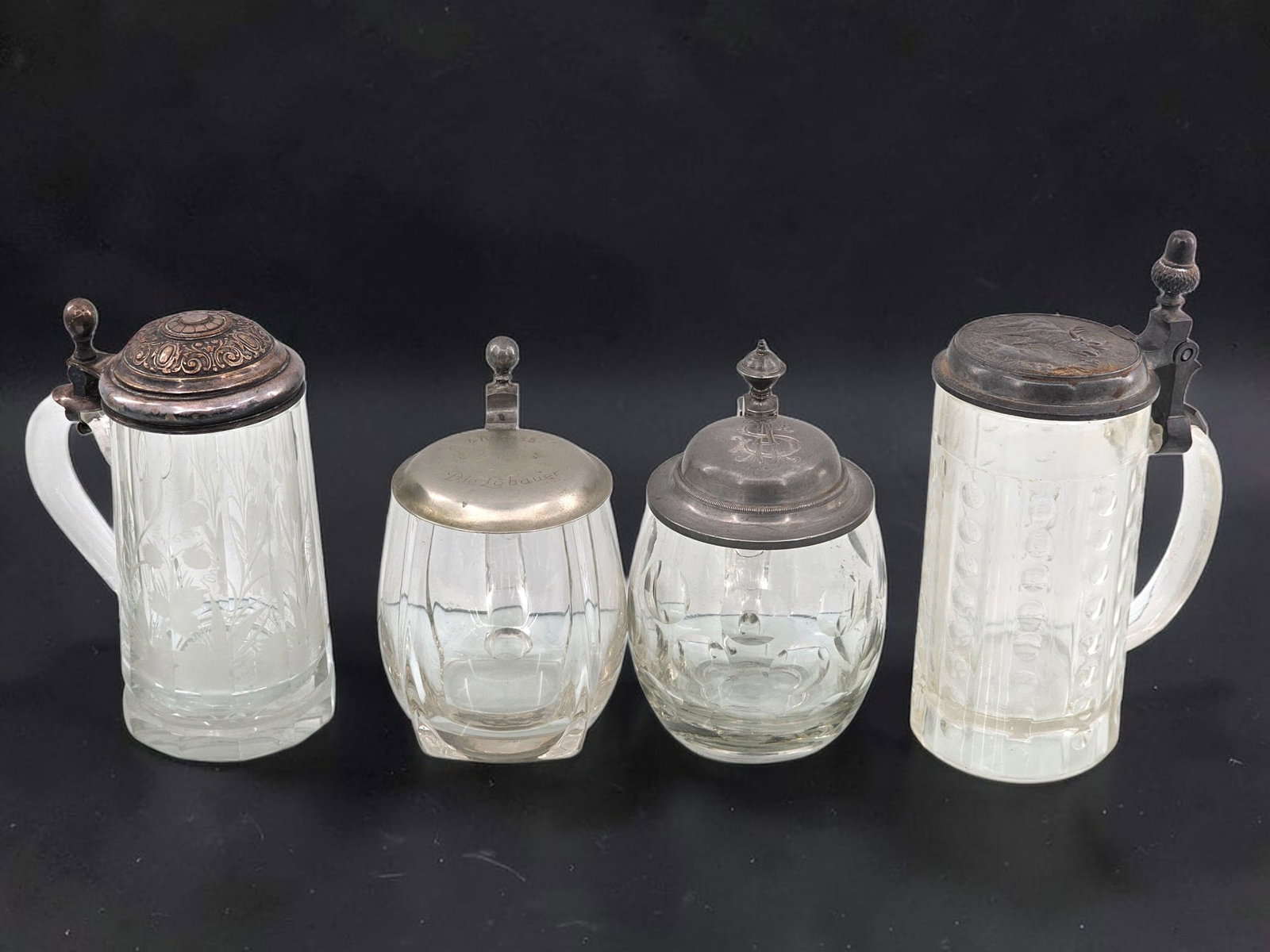 (4pc) Vintage Cut & Etched Glass Beer Steins: This lot includes four beer steins with cut and etched designs on clear glass. Each strain has a pewter lid and one appears to be monogrammed. Wear consistent with age and use including surface wear,