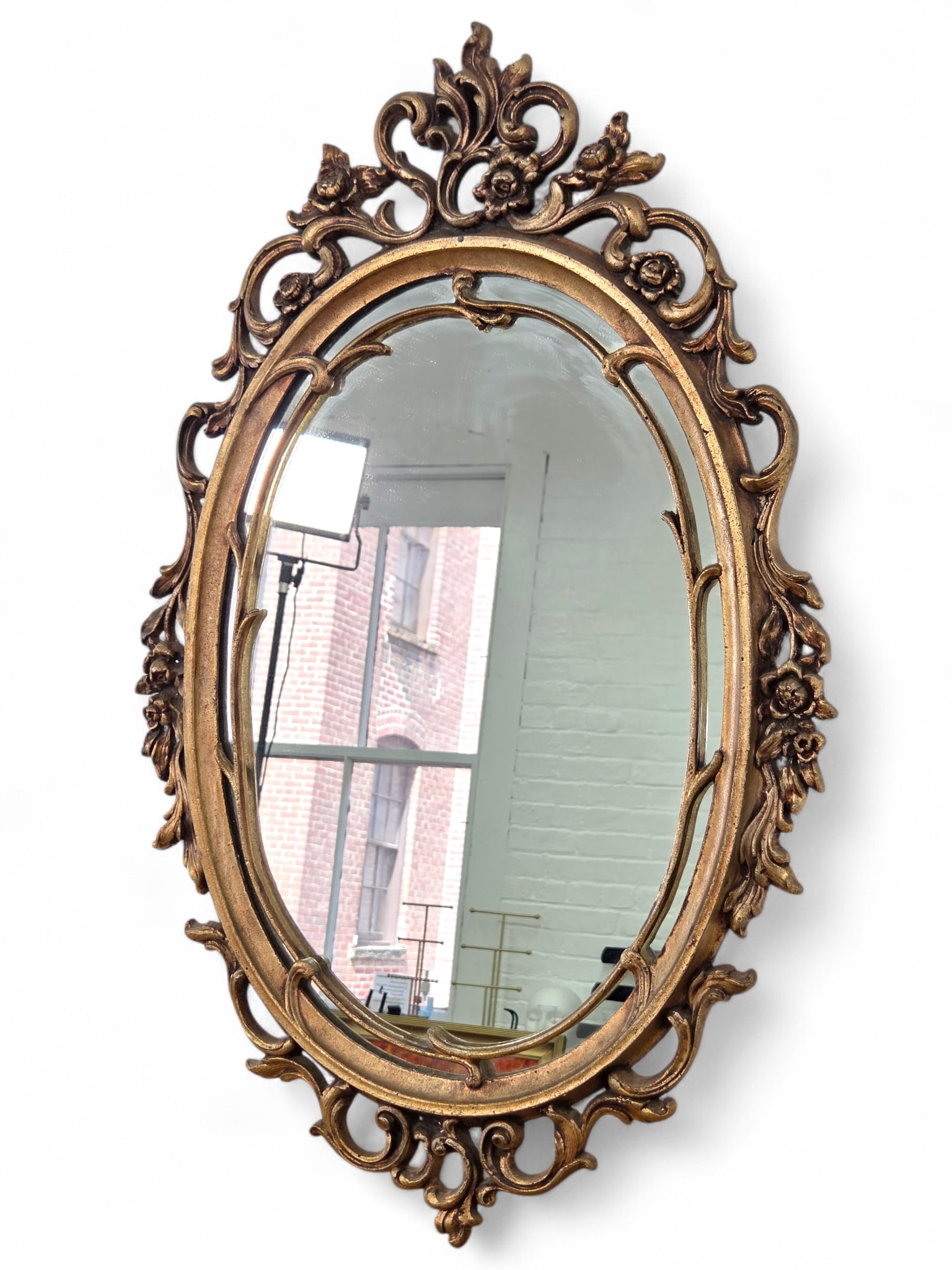 Ornate Cast Iron Oval Mirror: Oval wall mirror with gold-toned painted cast iron frame and ornate Victorian style scrolling details. Wear consistent with age and use including surface wear and oxidation. See photos for more item a