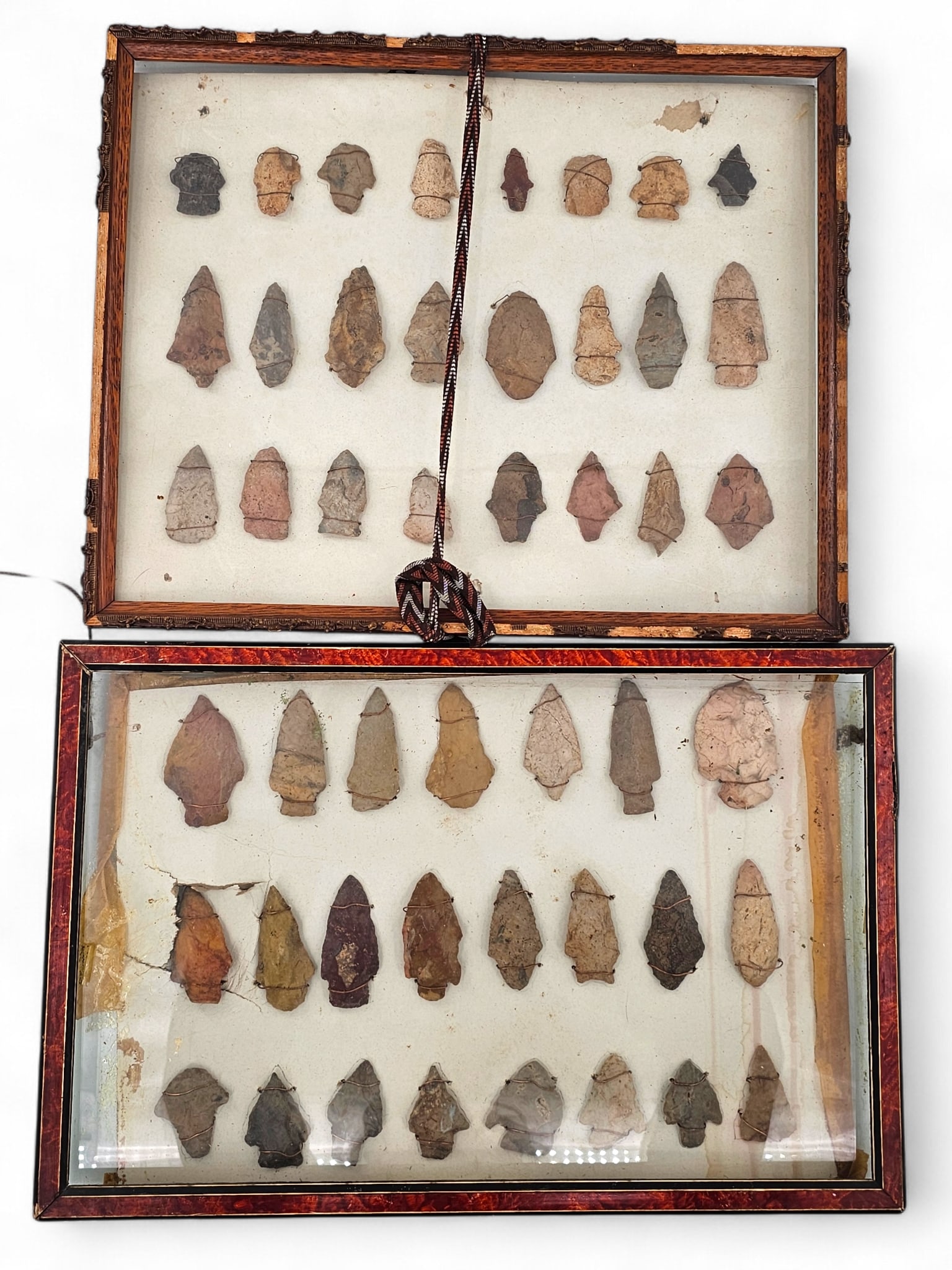 Pair of Framed Native American Stone Arrowhead Displays - 10 x 16: Pair of Native American arrowheads displays framed behind glass. displayed on board. Many with straight stems, expanding stems, and more. Both have loose glass and notably damaged frames and matting.