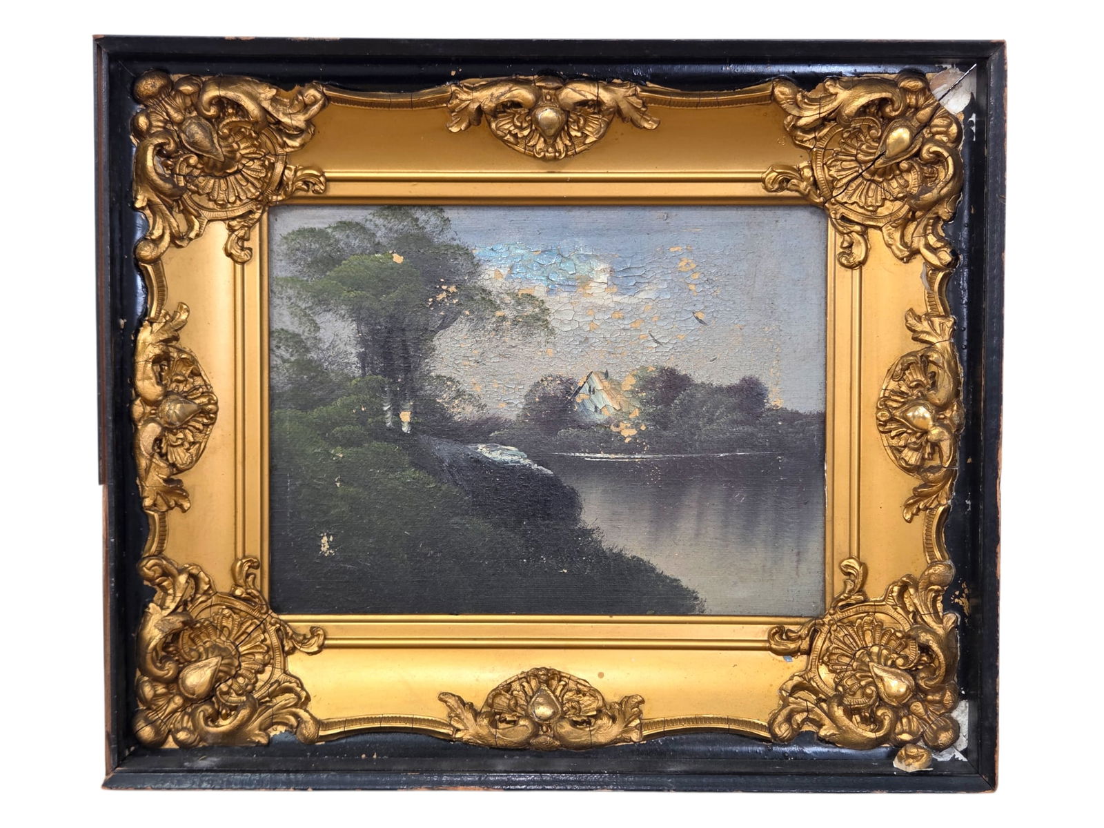 Landscape Oil Painting in Ornate Gilt Shadow Box Frame:  Oil Painting depicting a lakeside scene with a house. The painting is housed in a black shadowbox frame with an ornate moulded gilt interior. The painting has notable heavy flaking, losses, and