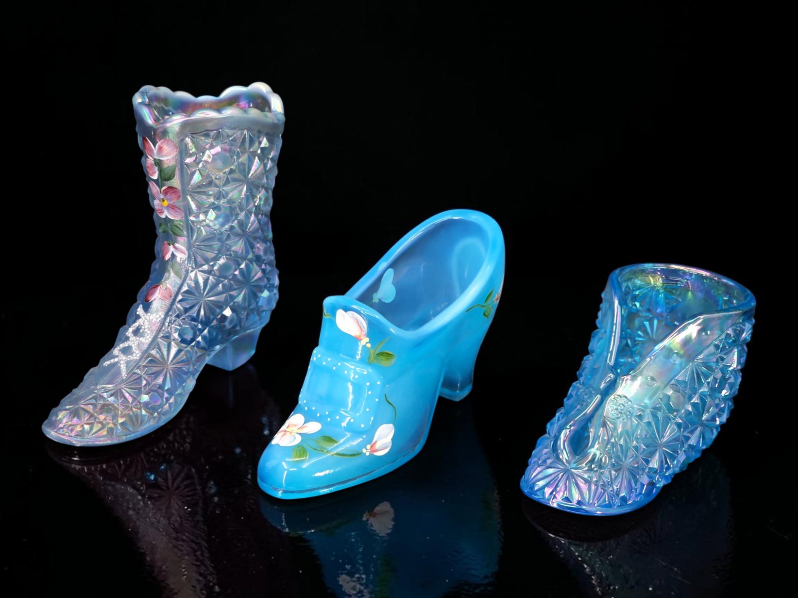 (3pc) Fenton Blue Carnival/Opaline Glass Shoes: Three Fenton shoe figurines, including a blue opaline glass slipper with hand painted flower decorations, a blue carnival glass slipper, and a light blue carnival glass boot with hand-painted flowers.