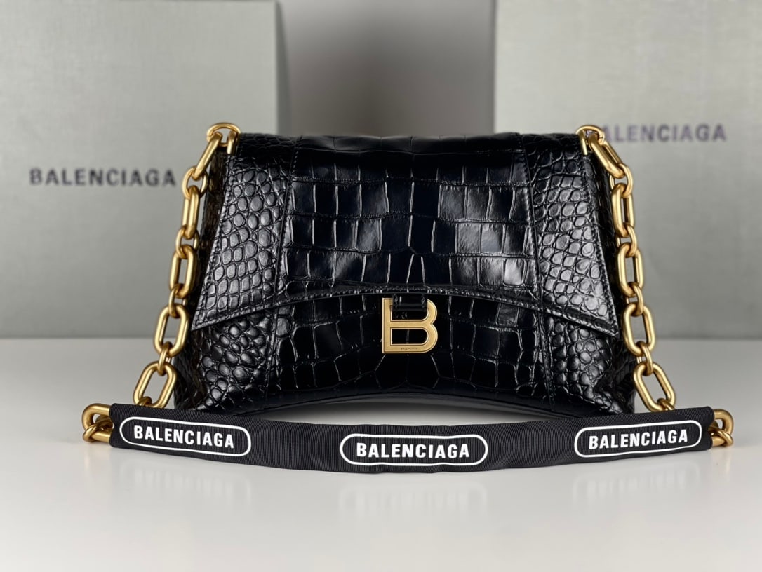 Balenciaga: The Balenciaga Downtown chain shoulder bag in black and gold with crocodile pattern features the same sharp angles and contours as the classic Hourglass design. The hardware and bicycle lock-like chai