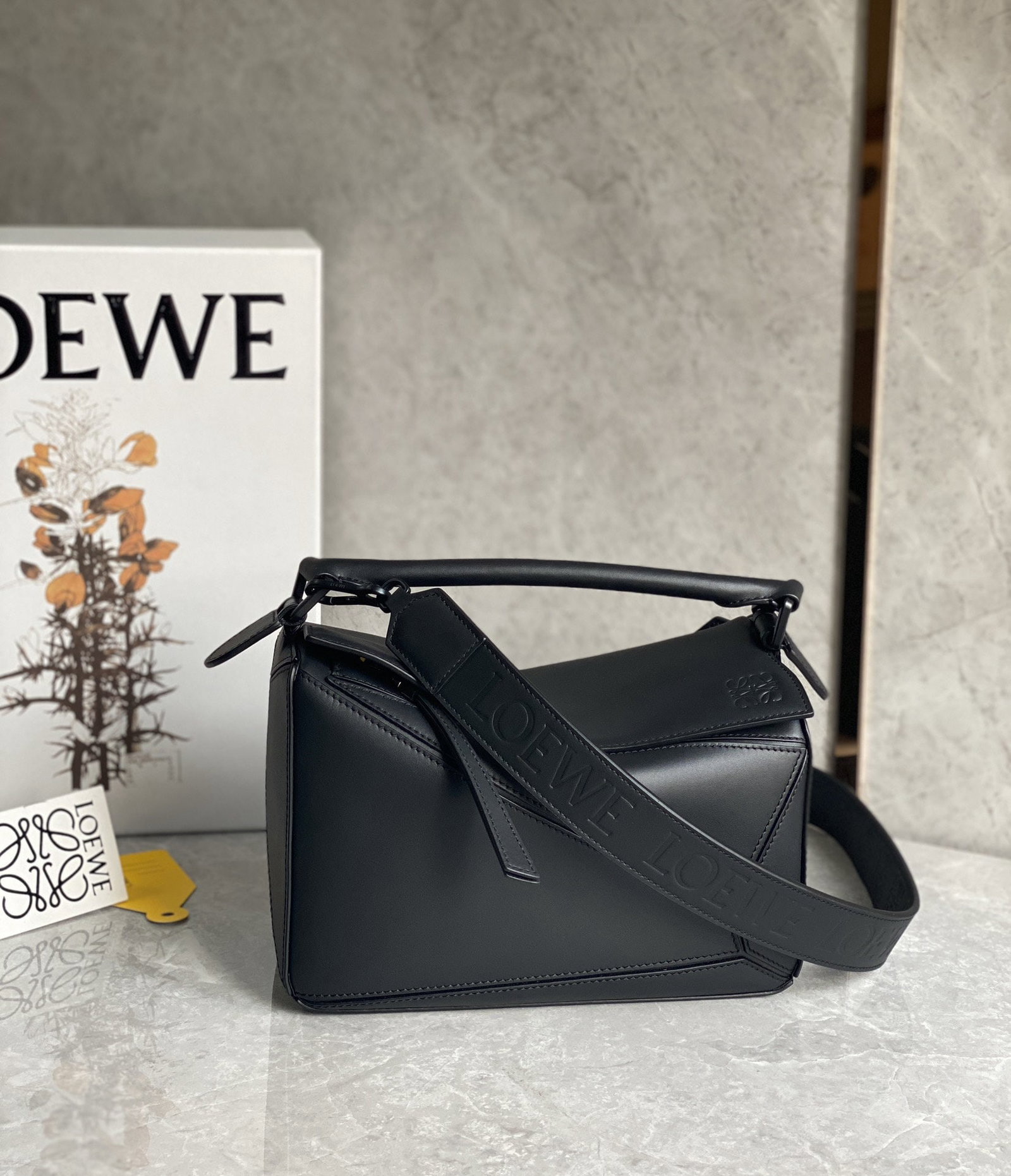 LOEWE: The LOEWE Puzzle in its cool black series is most notable for its satin finish cowhide leather, which is more delicate and lustrous than ever before. The shoulder strap, metal buckle, and lining are