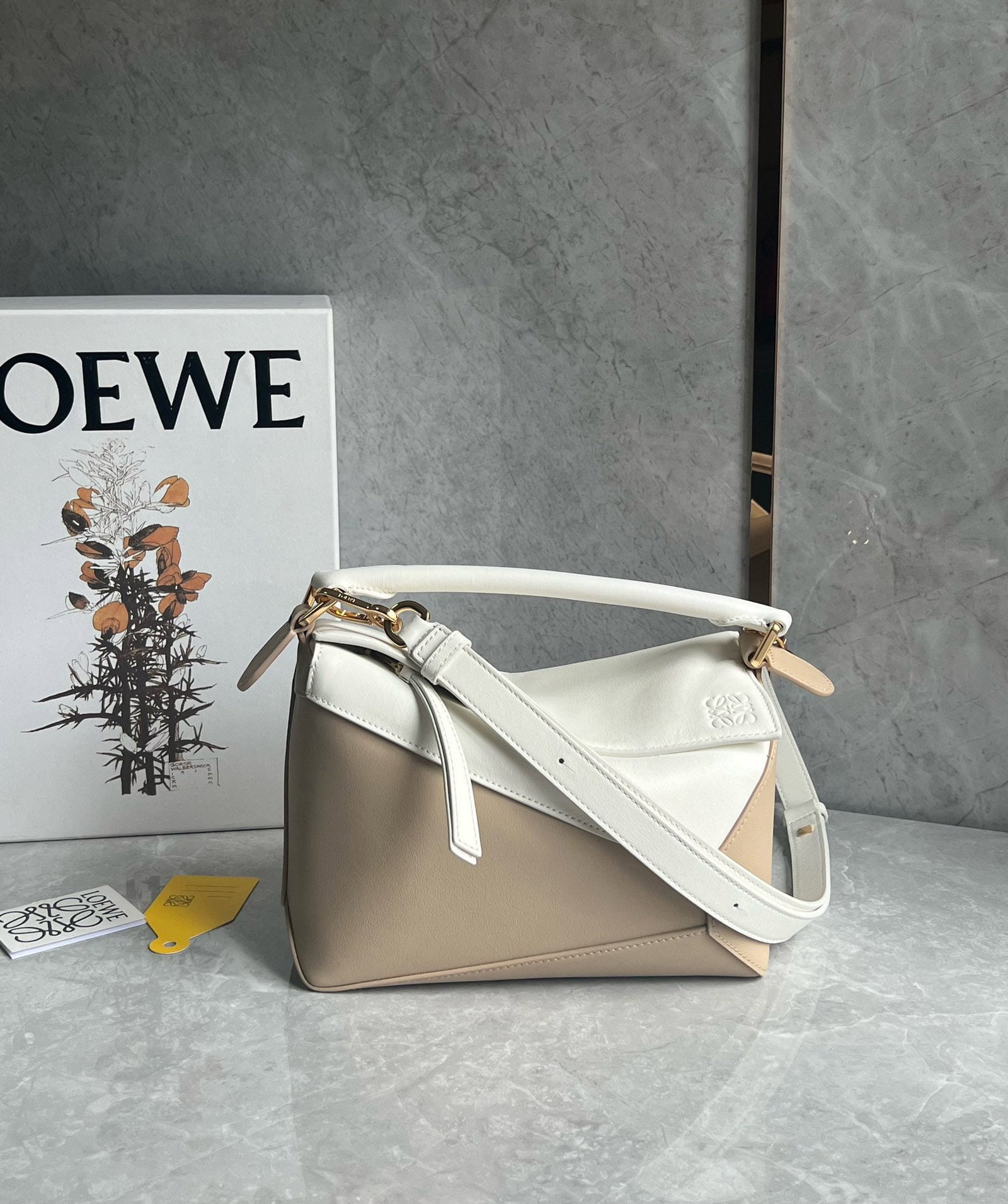LOEWE: The LOEWE Puzzle bag, in a creamy white color blocked design, is made of calfskin. It's lightweight yet surprisingly spacious, practical, versatile, and convenient for travel. Small size: 24 x 16 x