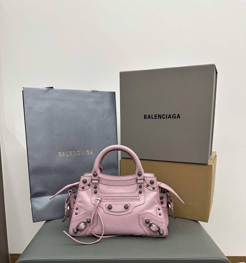 Balenciaga Neo Cagole Motorcycle Bag: This Balenciaga Neo Cagole motorcycle bag in a waxed cherry blossom pink comes with a heart shaped mirror. Beneath its cool and edgy exterior lies a sweet heart. Carrying it instantly elevates your en