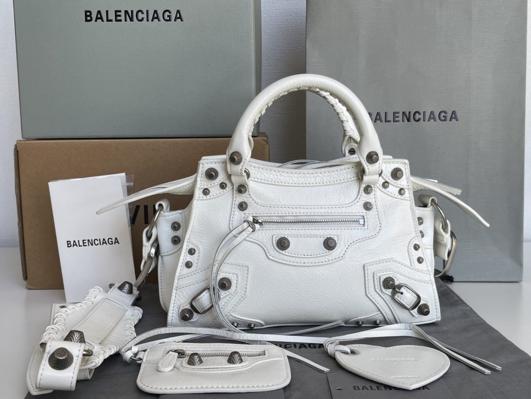 Balenciaga Neo Cagole Motorcycle Bag: This waxed white Balenciaga Neo cagole motorcycle bag features a heart shaped mirror. Beneath its cool and edgy exterior lies a sweet heart. Carrying it instantly elevates your entire aura. A must hav