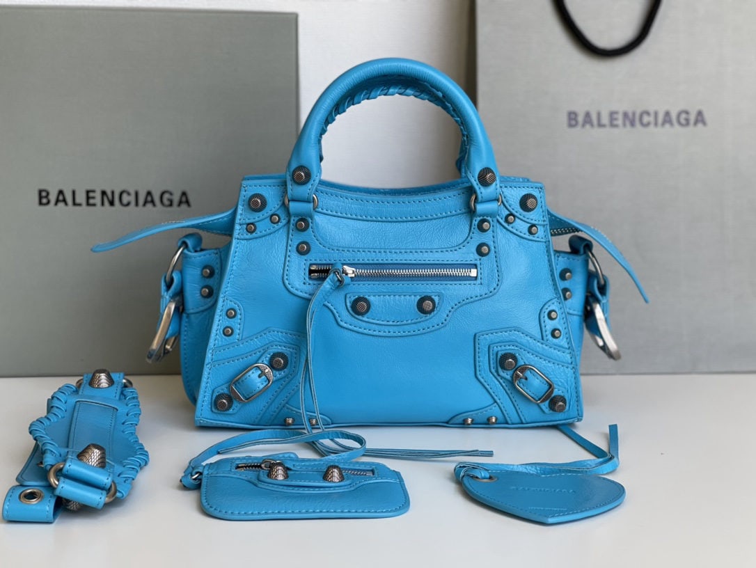 Balenciaga Neo Cagole Motorcycle Bag: This Balenciaga Neo Cagole motorcycle bag in waxed blue features a heart shaped mirror. Beneath its cool and edgy exterior lies a sweet heart. Carrying it instantly elevates your entire aura. A must h