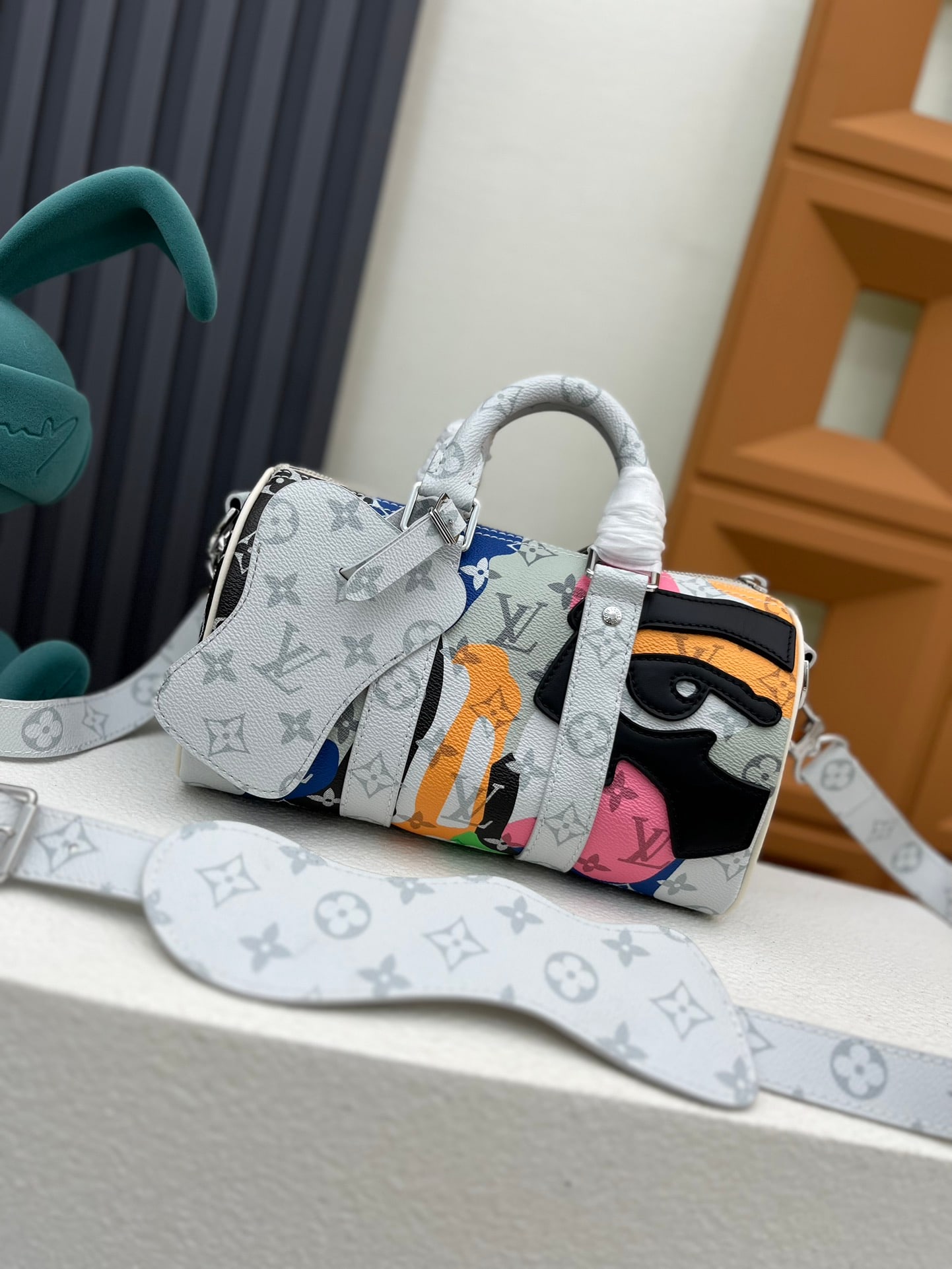 Keepall Bandouliere 25 handbag: This Keepall Bandouliere 25 handbag is from the LV Portrait collection, featuring leather patches and printed patterns, complemented by Monogram leather and canvas trim. 25.0 x 15.0 x 11.0 cm (Length