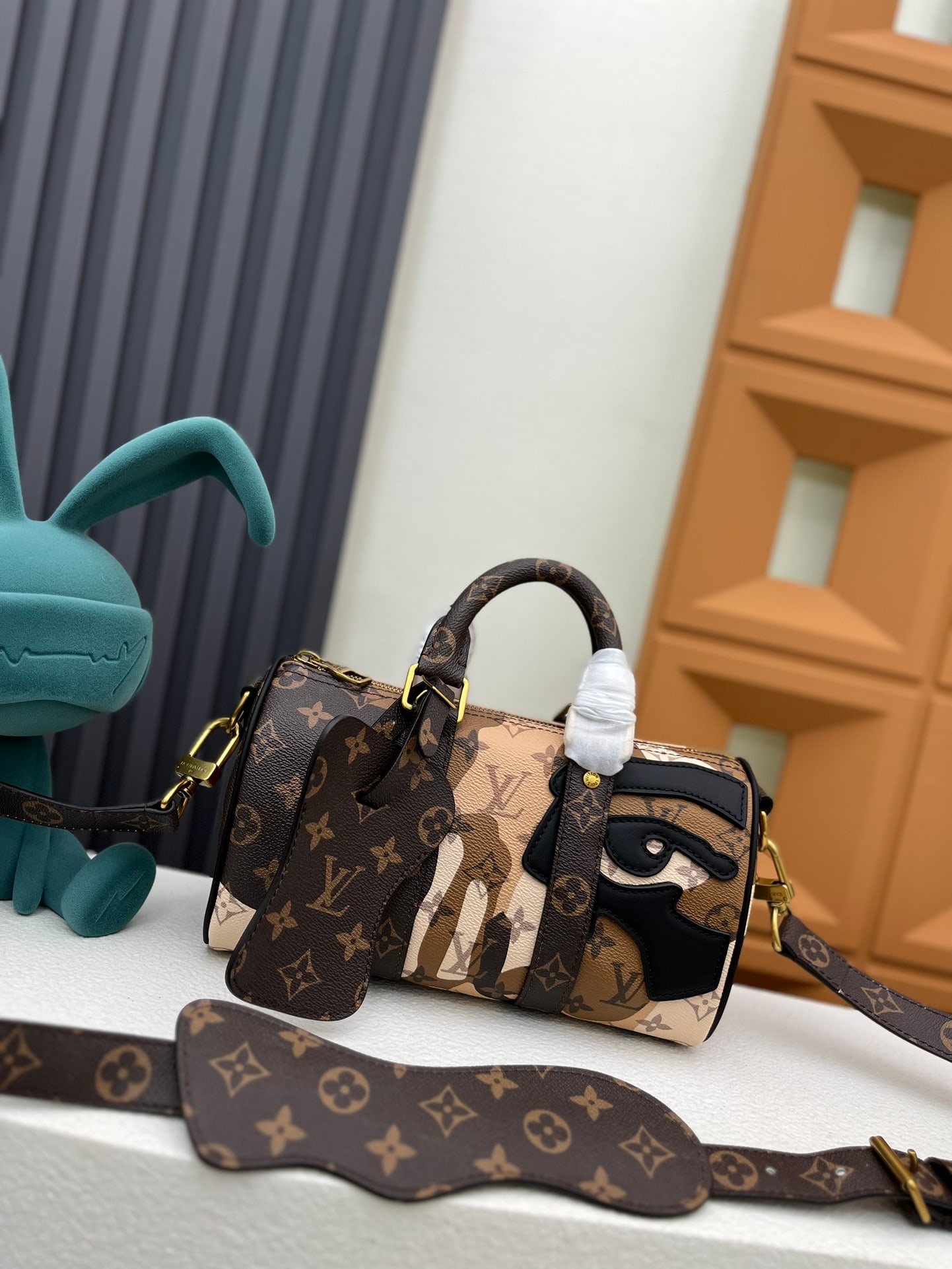 Keepall Bandouliere 25 handbag: This Keepall Bandouliere 25 handbag is from the LV Portrait collection, featuring leather patches and a seemingly printed pattern, complemented by Monogram leather and canvas trim. 25.0 x 15.0 x 11.0 