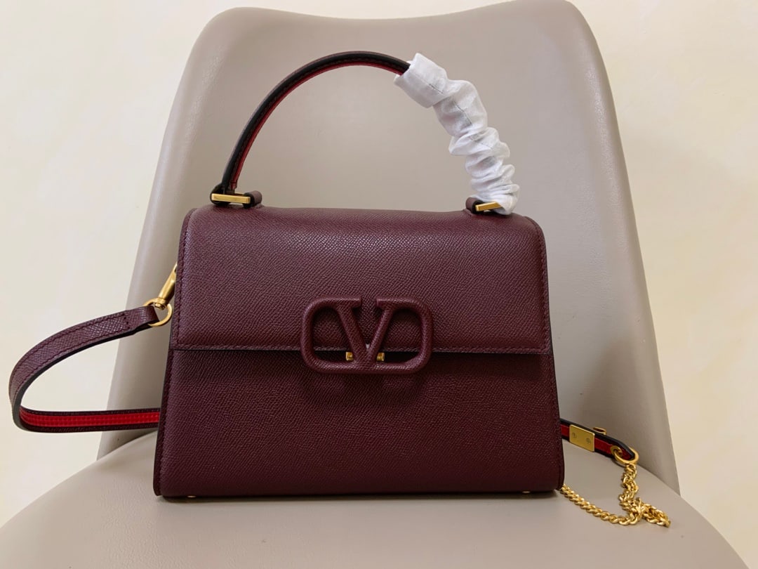 Valentino Garavani VSLING: This maroon Valentino Garavani VSLING briefcase features a palm print design and comes with an extendable two tone shoulder strap and handles. It can be easily worn over the shoulder, crossbody, or ca