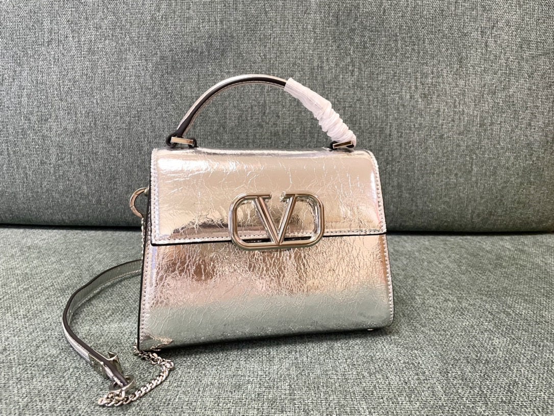 Valentino Garavani VSLING: The Papaya Silver Mini Valentino Garavani VSLING briefcase features a palm print design and comes with an extendable two tone shoulder strap and handle. It can be easily worn over the shoulder, crossb