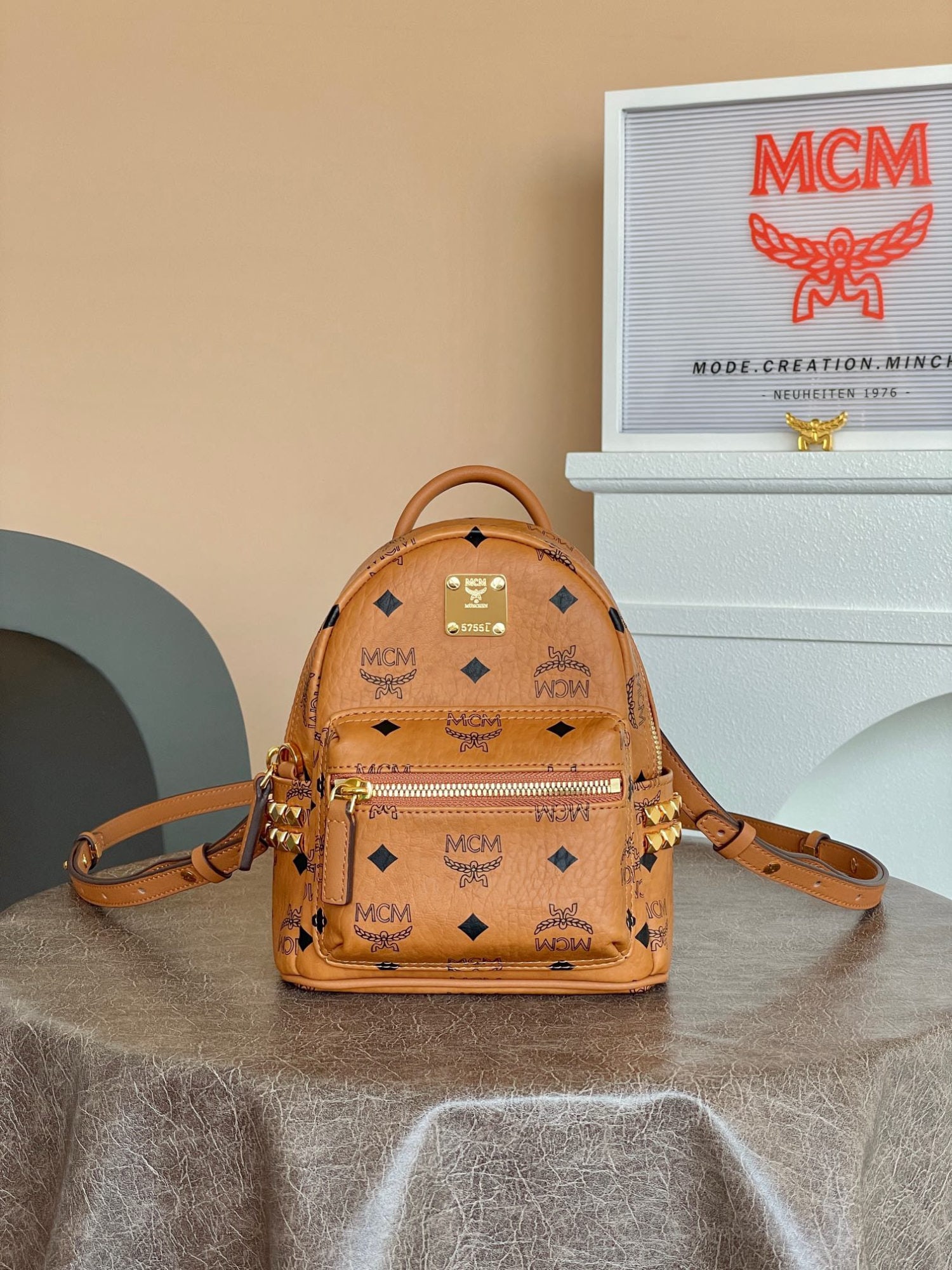 MCM Strak Visetos X-Mini Studded Backpack in Classic Cognac Color: The MCM Strak Visetos X-Mini Studded Backpack in classic cognac color showcases a fresh style with this ultra-mini Stark backpack. Crafted from classic Visetos, it features luxurious Nappa leather tri