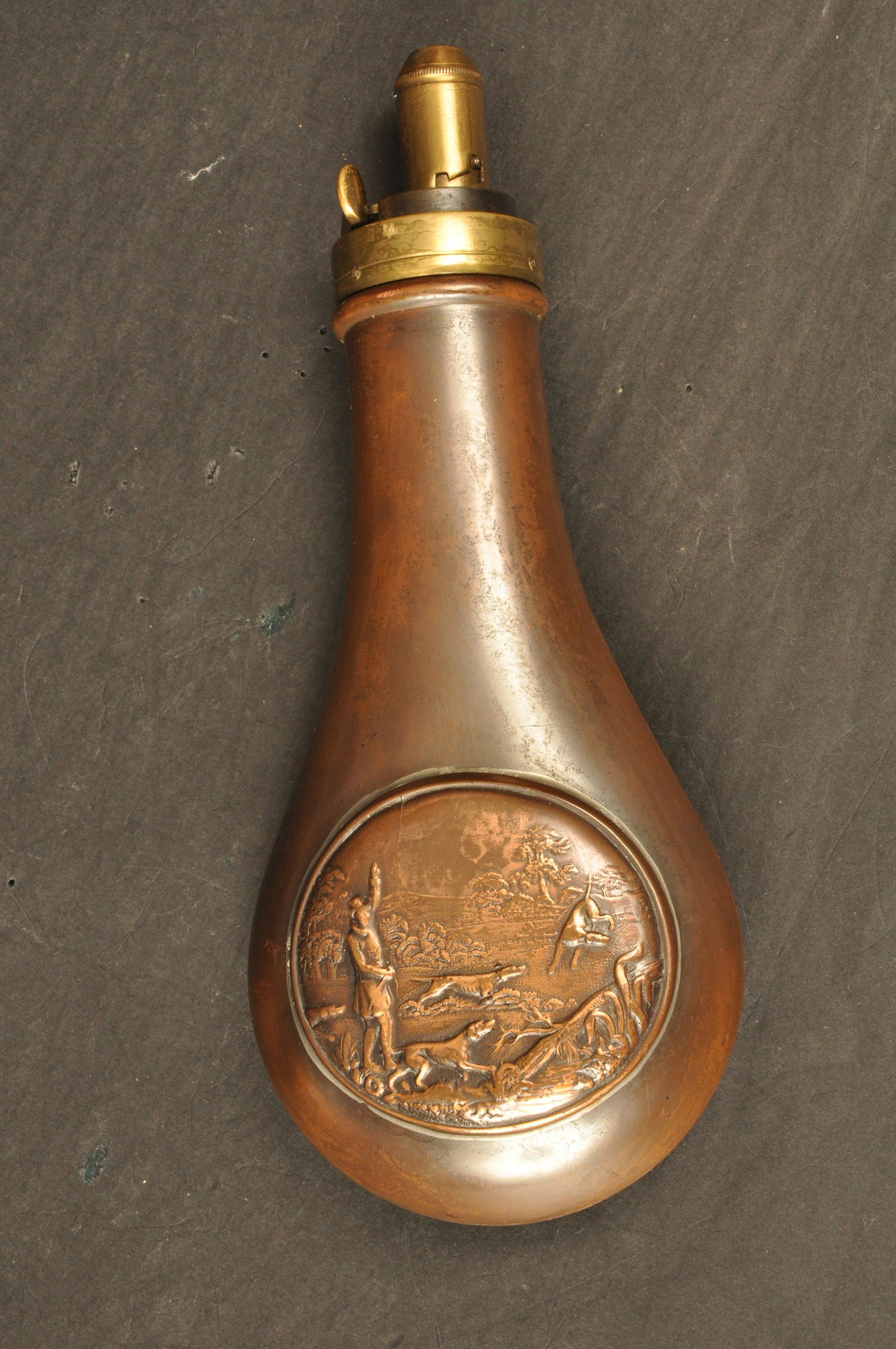 Powder Flask: Turn of the century, marked Made in England. Copper and brass with rounded embossed panel depicting a dog trainer & four english pointers. 7.5" OAL.