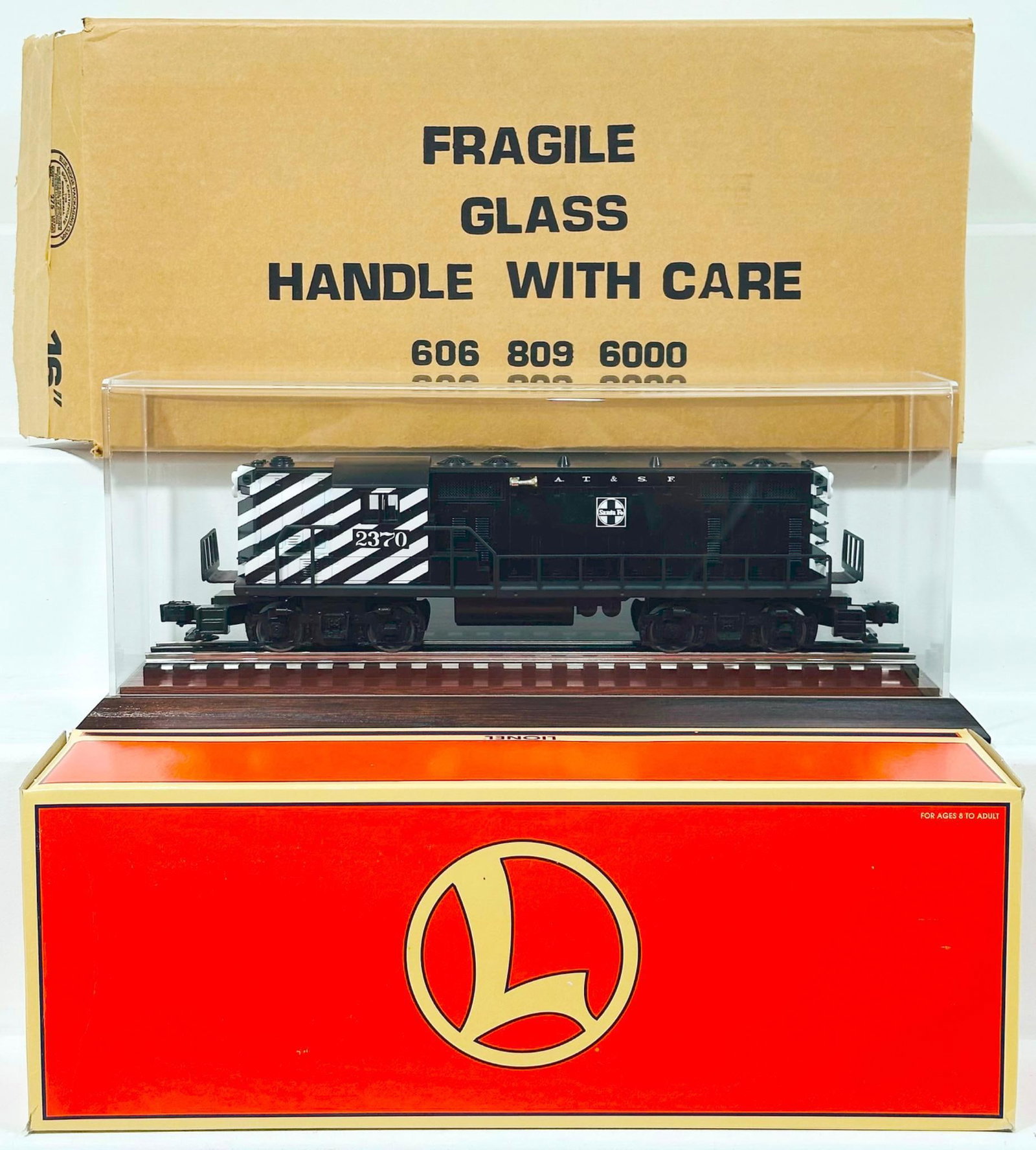 Lionel Modern O Gauge ATSF GP - 9 Diesel Switcher Boxed with Plexiglass Showcase: Lionel Modern O Gauge ATSF GP - 9 Diesel Switcher Boxed with Plexiglass Showcase, in C9 and with its original box. This Lot also includes a plexiglass showcase with wood/track base.