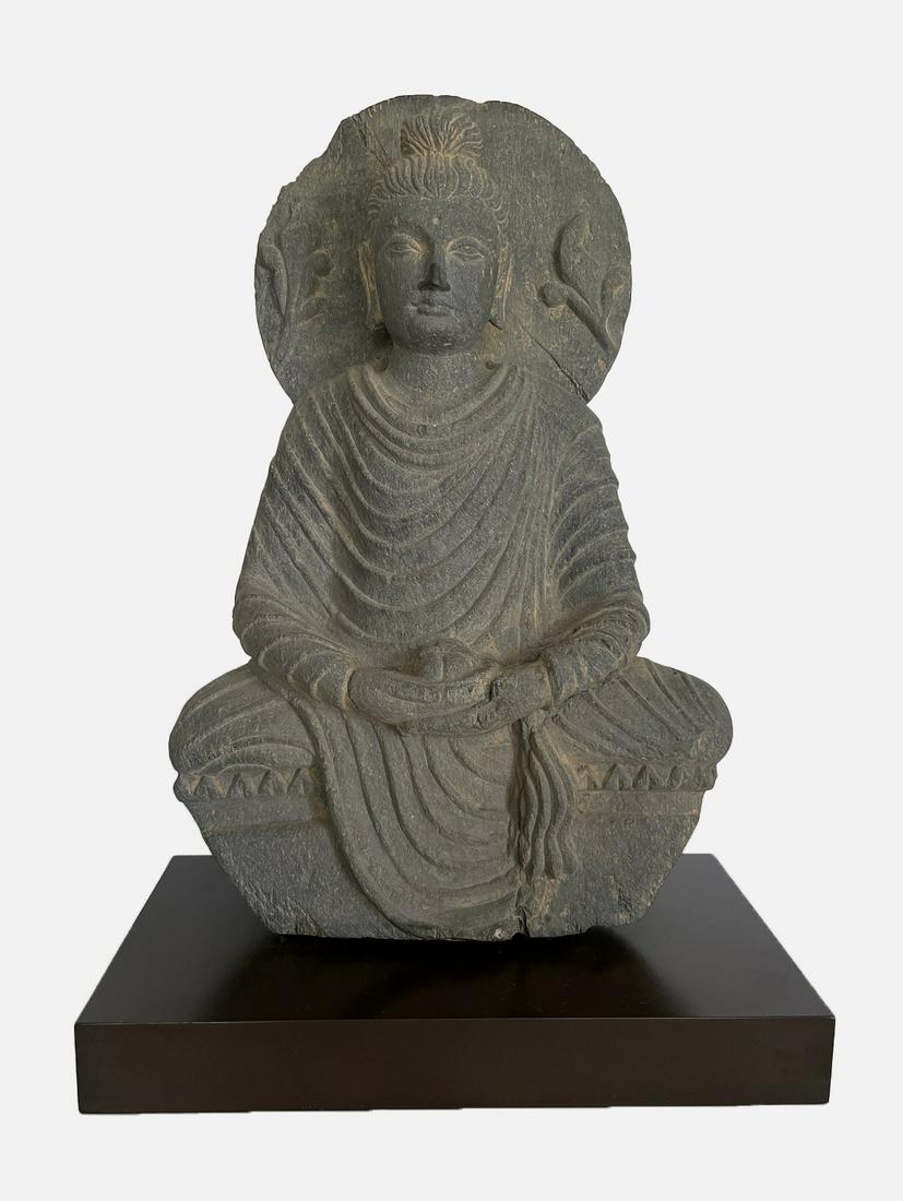 A Gray Schist Figure of Buddha, ca 2nd - 3rd century: A Gray Schist Figure of Buddha Gandhara , circa 2nd to 3rd century 40.6 cm high Seated in dhyansana with two of his hands in dhayanamudra and wearing a flowing sanghati, his meditative face with heavy