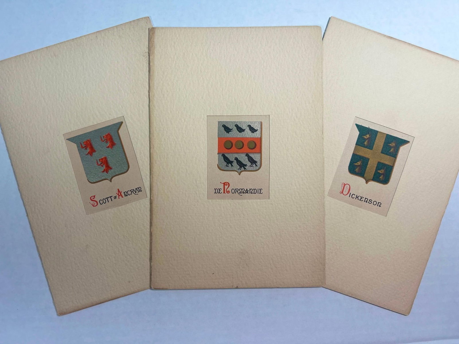 Three Miniature Family Crest Lithographs: Lot of 3 miniature family crest lithographs with origin descriptions. Markings on Miner left from tape. Booklet measures 9 1/4" x 6 1/4" Overall good condition.