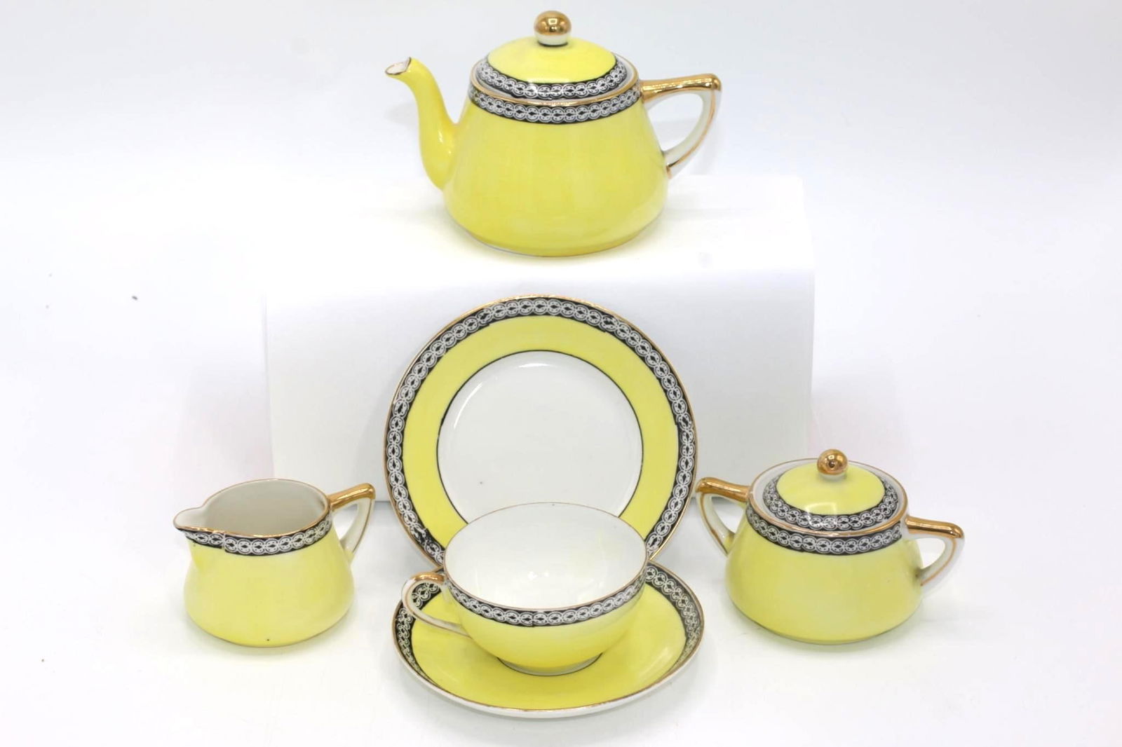 A Yellow Noritake Child's Tea Set: Japan, 20th century. A lovely child's tea set in yellow, black and white with gold detailing. Overall good condition; no chips present. 1 teapot 1 creamer 1 sugar 5 teacups 5 saucers 5 plates
