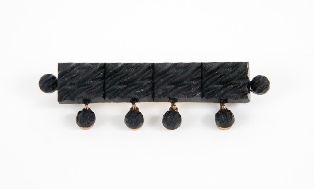 Victorian Crepe Stone Bar Pin: Victorian bar pin featuring carved black glass "crepe stone" consisting of four rectangular panels with matching bezel set dangles below. Mounted on rose gold with yellow gold pin and clasp. Size: 2.2