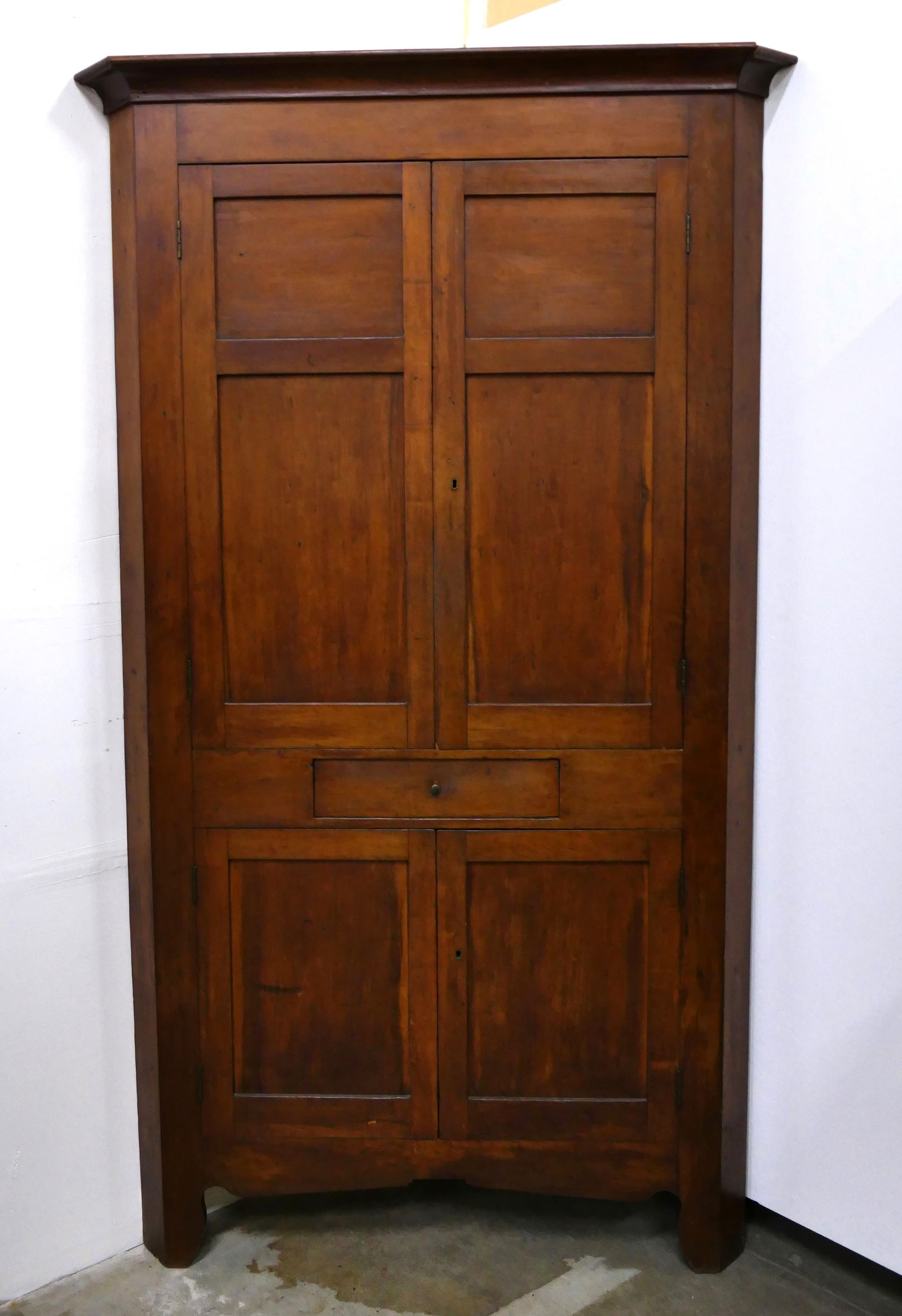 Antique Solid Cherry Corner Cupboard: Circa early 1800's antique solid cherry hand made single-piece corner cupboard featuring molded cornice, double panel blind doors, and hand-chamfered backs. There are triple stationary interior shelve