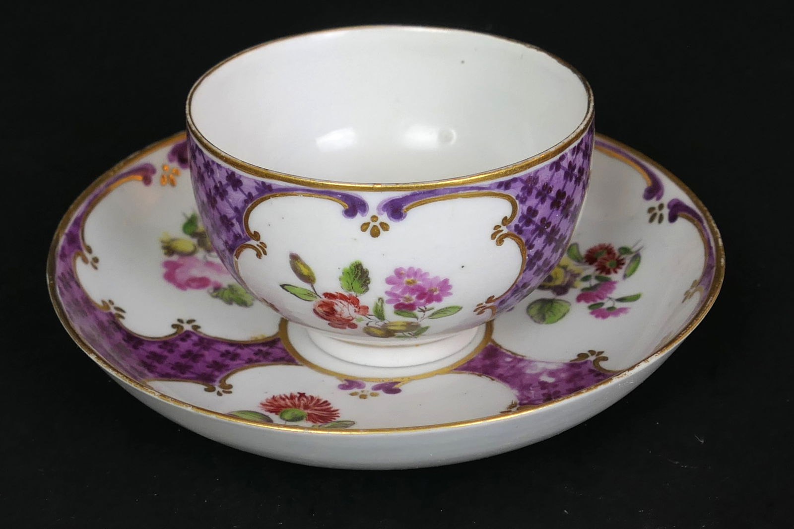Antique Cozzi Tea Bowl and Saucer: Circa 1770 tea bowl and saucer by Cozzi, Italy (Venice made), each painted in colorful floral sprays with three gilt-edged panels reserved on a ground of purple trelliswork, with the rims also edged i
