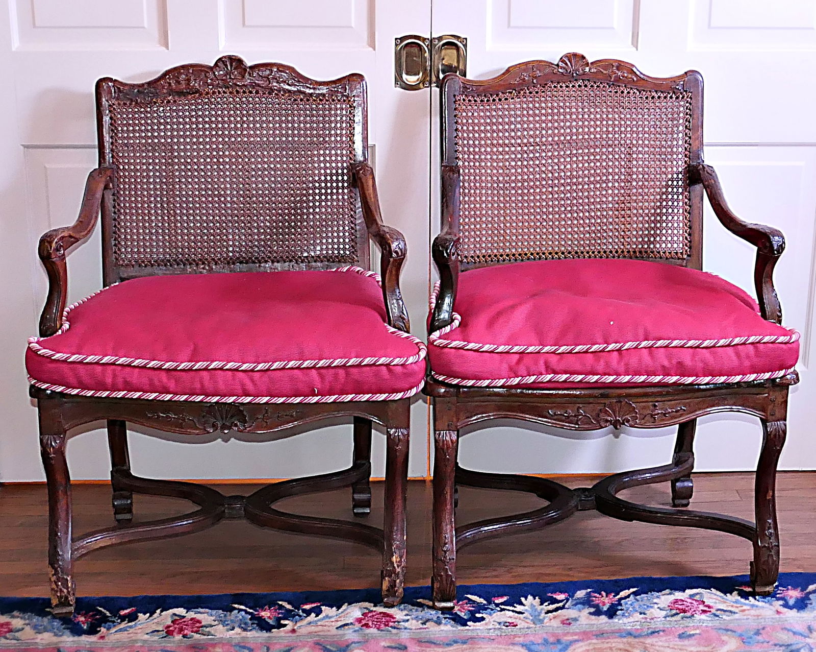 Antique Regency Walnut Armchair Pair: Circa 1725 regency walnut hand-carved armchair pair featuring caned backs and seats inside highly carved frames showing shell and foliate chair rails, carved arms, legs, and aprons with criss-cross lo