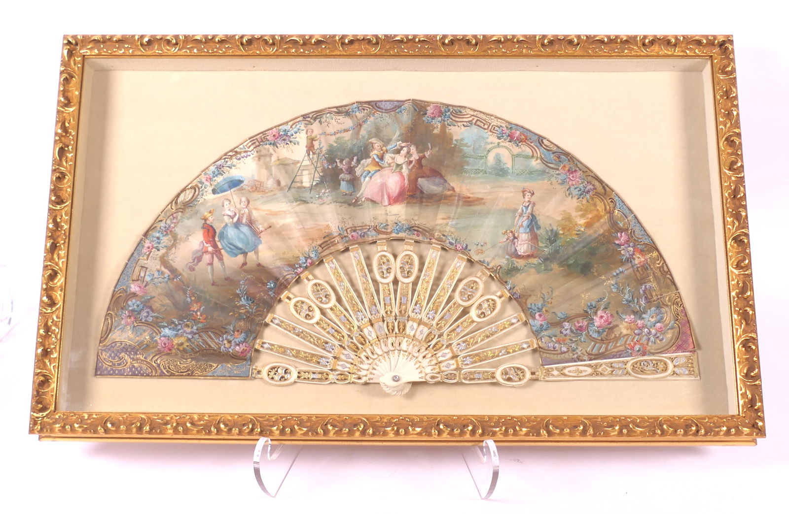 Framed Antique Hand Fan: Circa 18th century hand fan featuring bone sticks with carved and pierced floral motifs and hand painted courtship scenes with gilt accents throughout. Displayed in gold tone shadow box frame. Some te