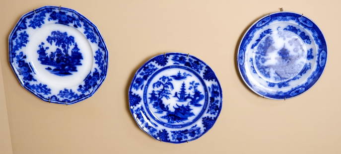 Three Blue and White Transferware Plates: Three vintage blue and white plates, each with a distinct scenic design and floral border, showcasing traditional motifs and craftsmanship. One round plate features a detailed landscape scene, an octa