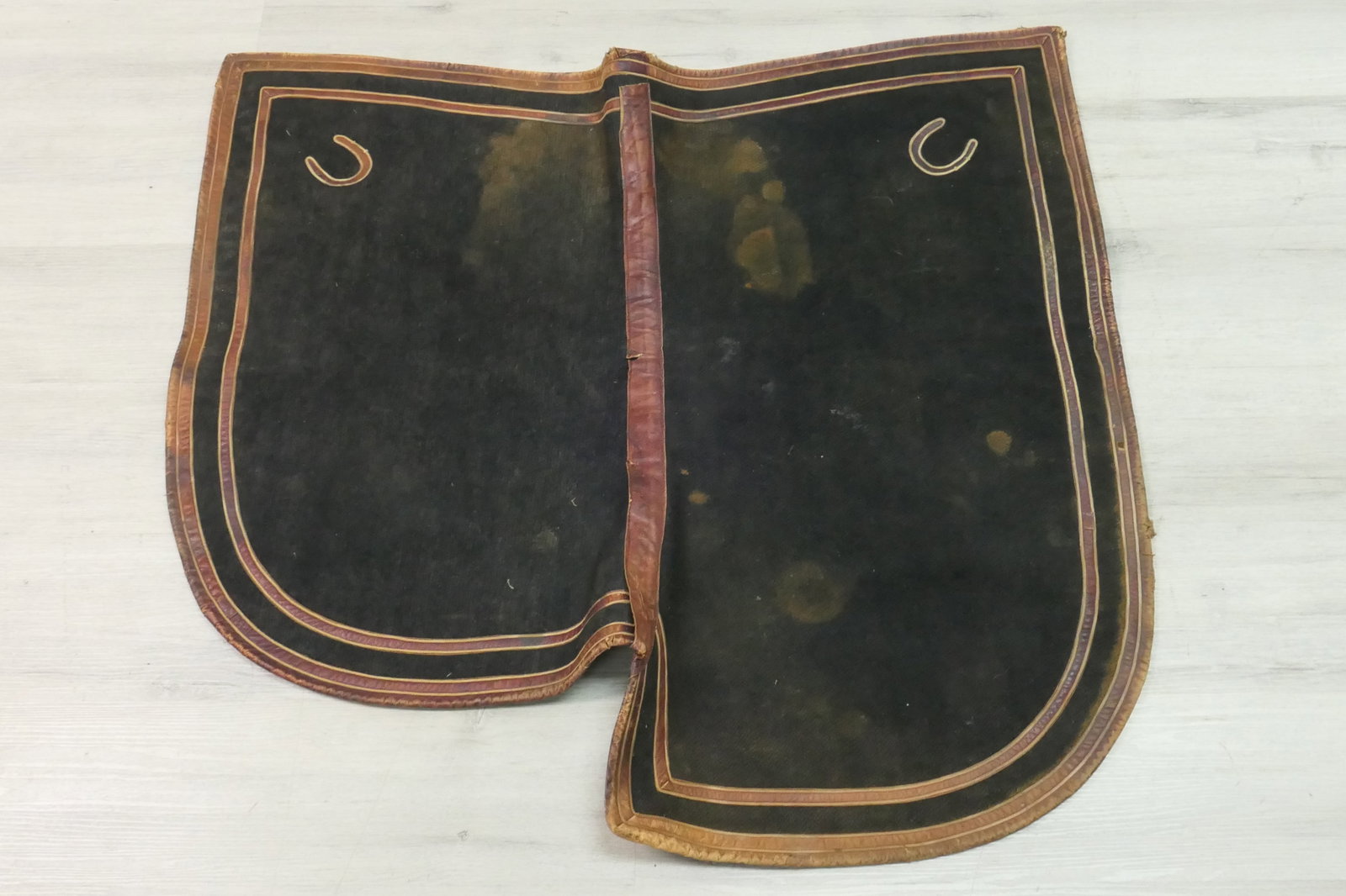 Saddle Blanket: Saddle blanket in green wool trimmed in leather. Leather is cracked, hole. Size: 34.5"w x 30.5"h