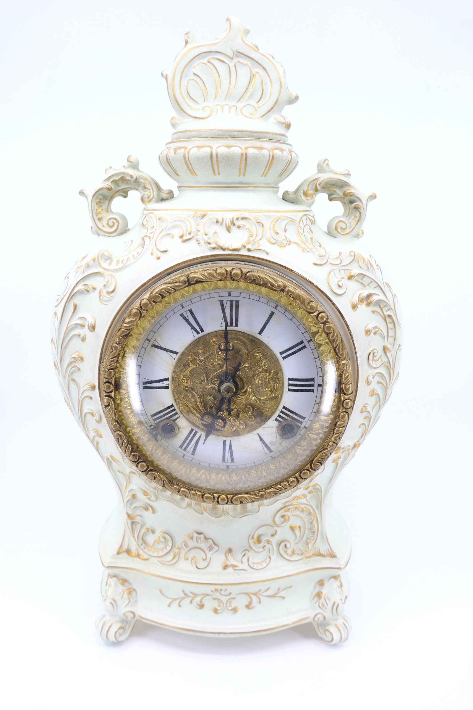 Louis XV Style Ornate Mantle Clock: Pale green urn style Louis XV ornate mantle clock with gilt accenting. Key and pendulum present. Repair to back top. Enamel face crack with touched up gold rim on glass door. Over wound. Size: 7.5"w x