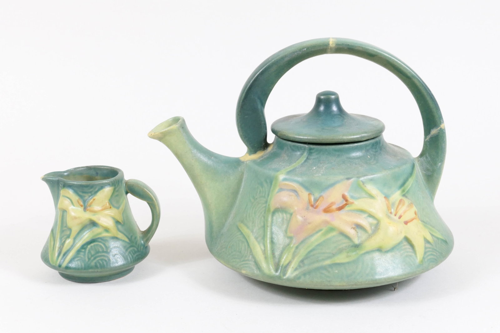 Roseville Zephyr Lily Teapot and Creamer: Roseville Zephyr Lily teapot and creamer featuring yellow and pink lilies on blue field with geometric motifs. The teapot is marked Roseville 7-7. The teapot handle has been broken and repaired in thr