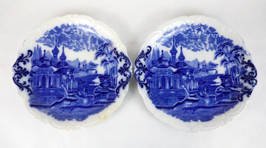 Two English Flow Blue Dishes: Two english flow blue dishes featuring architecture, clouds and scroll motifs. There is a white scroll textured edge. One shows a partial mark, believed to be James Kent, circa early 1900's. There is