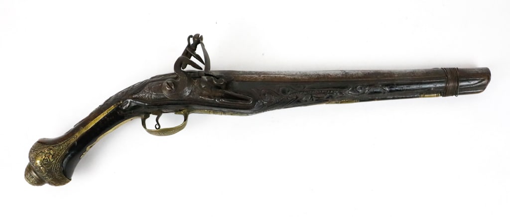 Turkish Ottoman Flintlock Pistol: Turkish Ottoman flintlock holster pistol with a carved walnut stock. Featuring a damascus round iron barrel, with engraved brass mounds. There is wrapped wire appearing to be non-original near the end