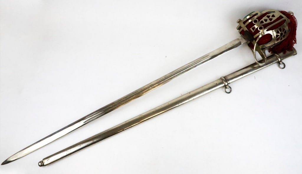 Scottish Basket Hilt Sword with Red Tassel: Scottish basket hilt sword with a silvertone pierced design, with a fitted pocket to protect your hand from contact. There is a leather handle with a braided brass wire and finial pommel with a red ta