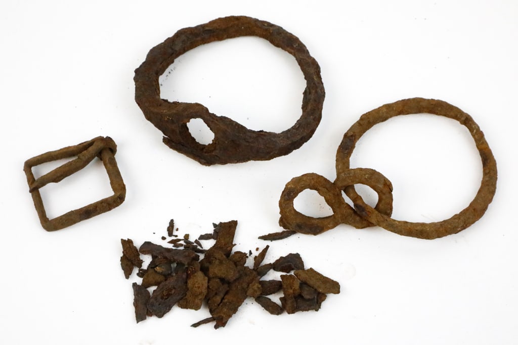 Iron Artifacts: Iron artifacts, including a buckle, two circular rings, and more. The pieces are presented in a bag marked medieval iron artifacts. The artifacts are oxidized to the point of breaking down. Size: 2.5"