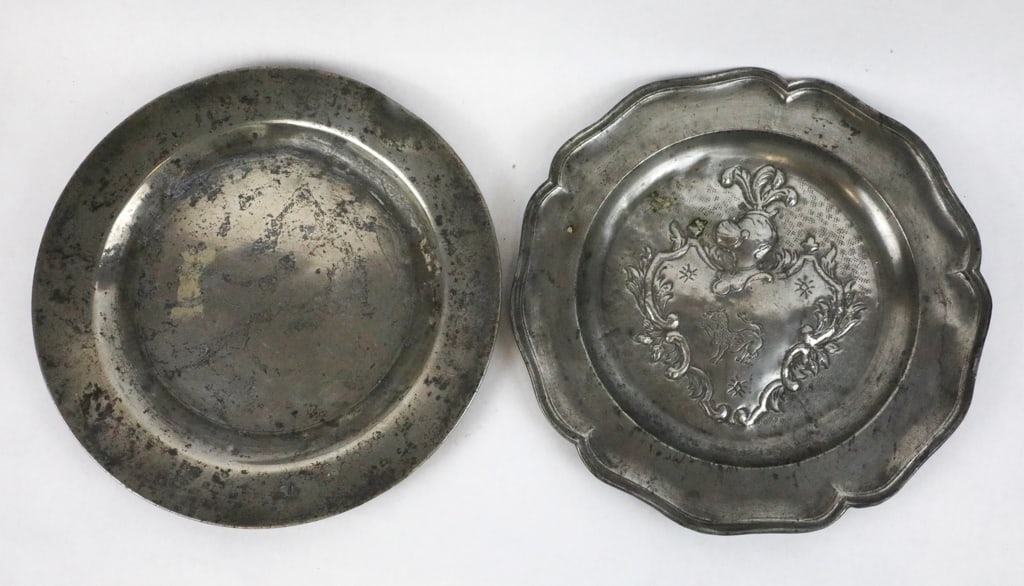 Two Pewter Plates: One with an Embossed Crest of a Knight and Shield and One with TS on the Rim: Two pewter plates: One plate is embossed with a crest insignia showing a scroll edged shield and feathered knight helmet inside a scalloped plate edge. Plate has three maker's hallmarks on the back an
