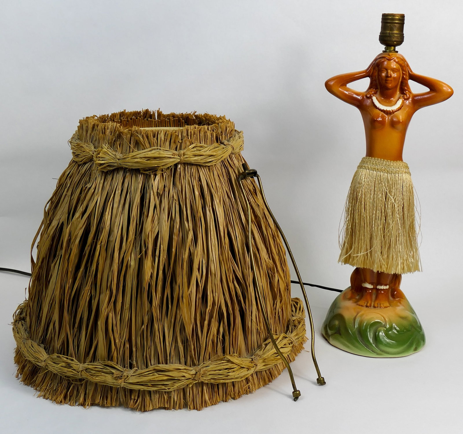 Ceramic Tropical Hula Lamp: Tropical hula lady lamp featuring a green swirled base and a figural statue post with a fiber tassel skirt, and a single socket rising from her head. The hips of this topless figure contain a