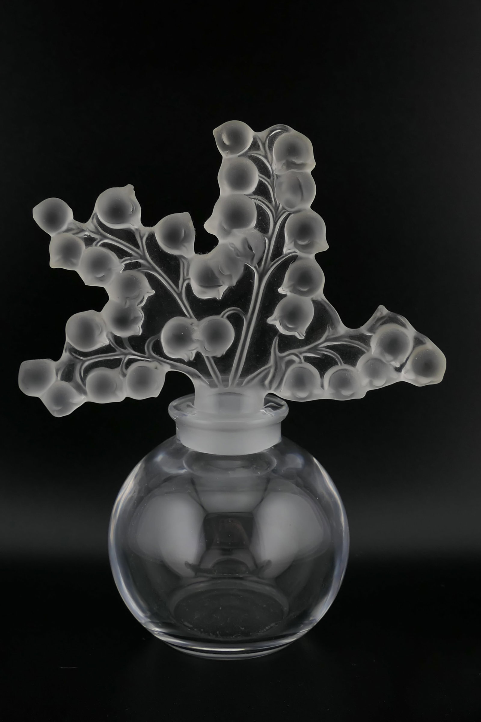 Lalique Crystal Claire Fontaine Perfume Bottle: Lalique crystal perfume bottle in the Claire Fontaine pattern featuring an ornate frosted crystal stopper with a lily of the valley motif. Excellent condition. Size: 4.75"h Location: Living Room