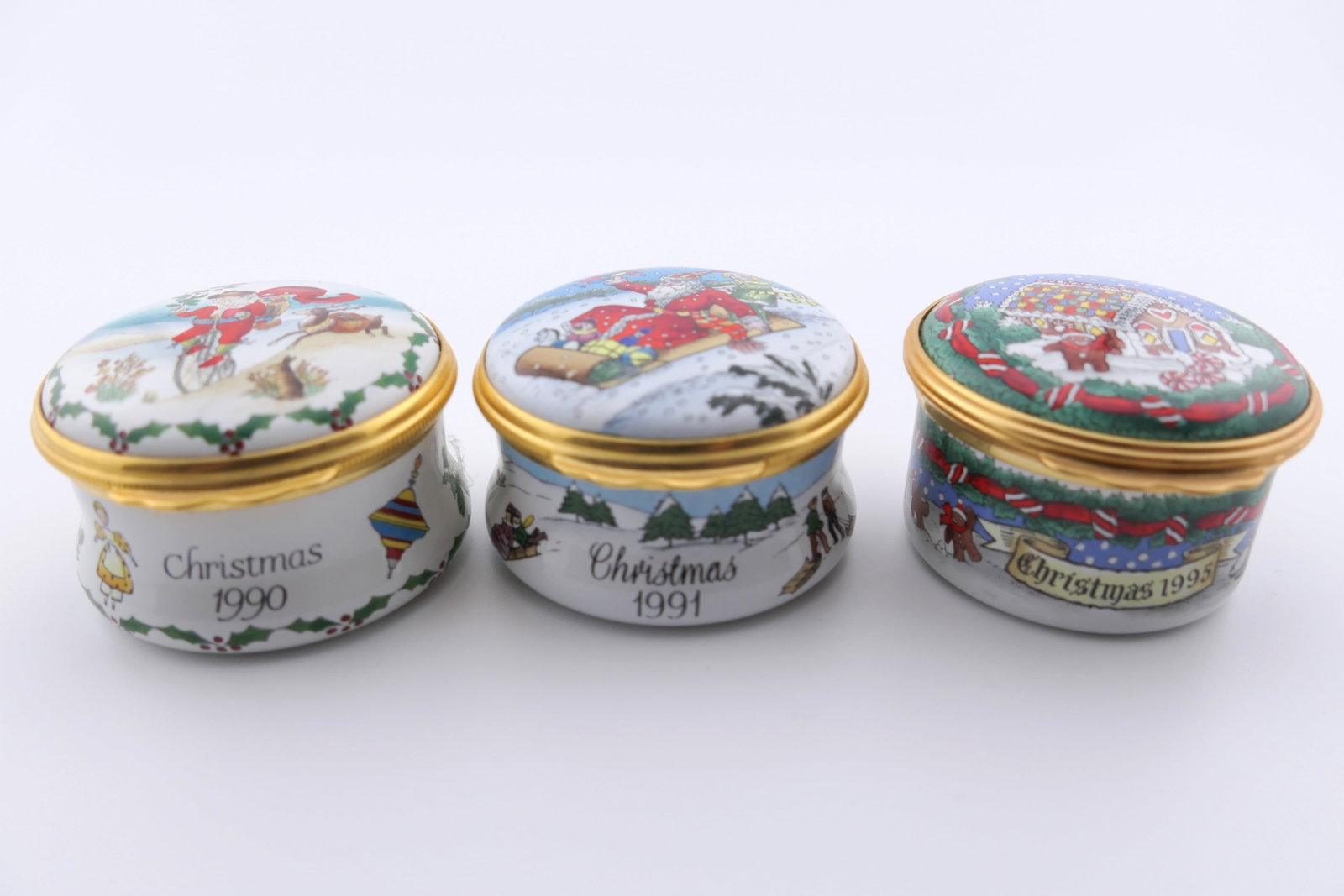 Halcyon Days Christmas Trinket Box Trio: Trio of marked Halcyon Days Christmas hinged trinket boxes for the years 1990, 1991, 1995, featuring festive holly and ribbon motifs. Two are marked Smithsonian Institution, one is marked Neiman Marcu