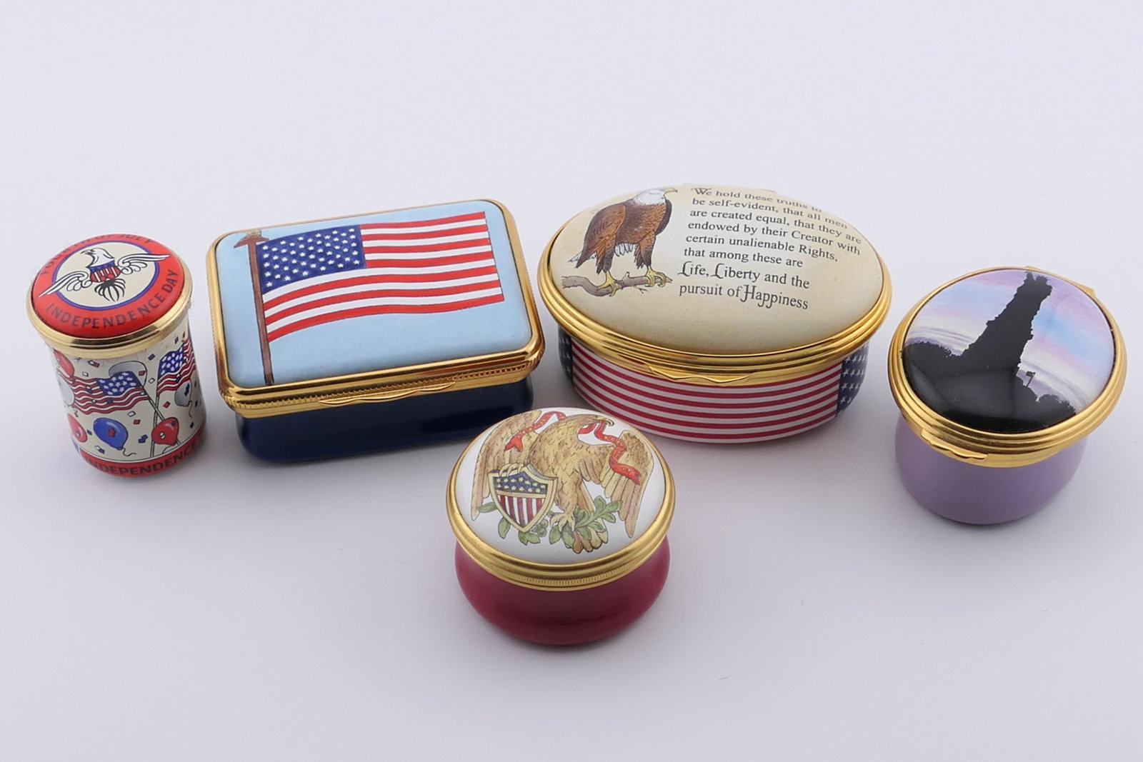 Patriotic Halcyon Days Trinket Boxes: Five marked Halcyon Days trinket boxes featuring patriotic designs such as flags, eagle, Statue of Liberty, and more. All are marked Halcyon Days Enamels. One lid is hinged, two twist off. Very good c