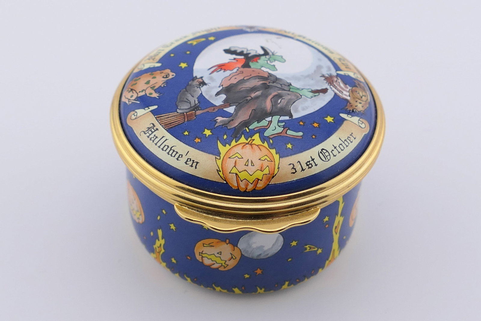 Halcyon Days All Hallows Eve Trinket Box: Marked Halcyon Days hinged trinket box in the All Hallows Eve pattern, featuring a witch motif on the lid. Marked on the bottom Halcyon Days Enamels with original box. Excellent condition. Size: 1.75"