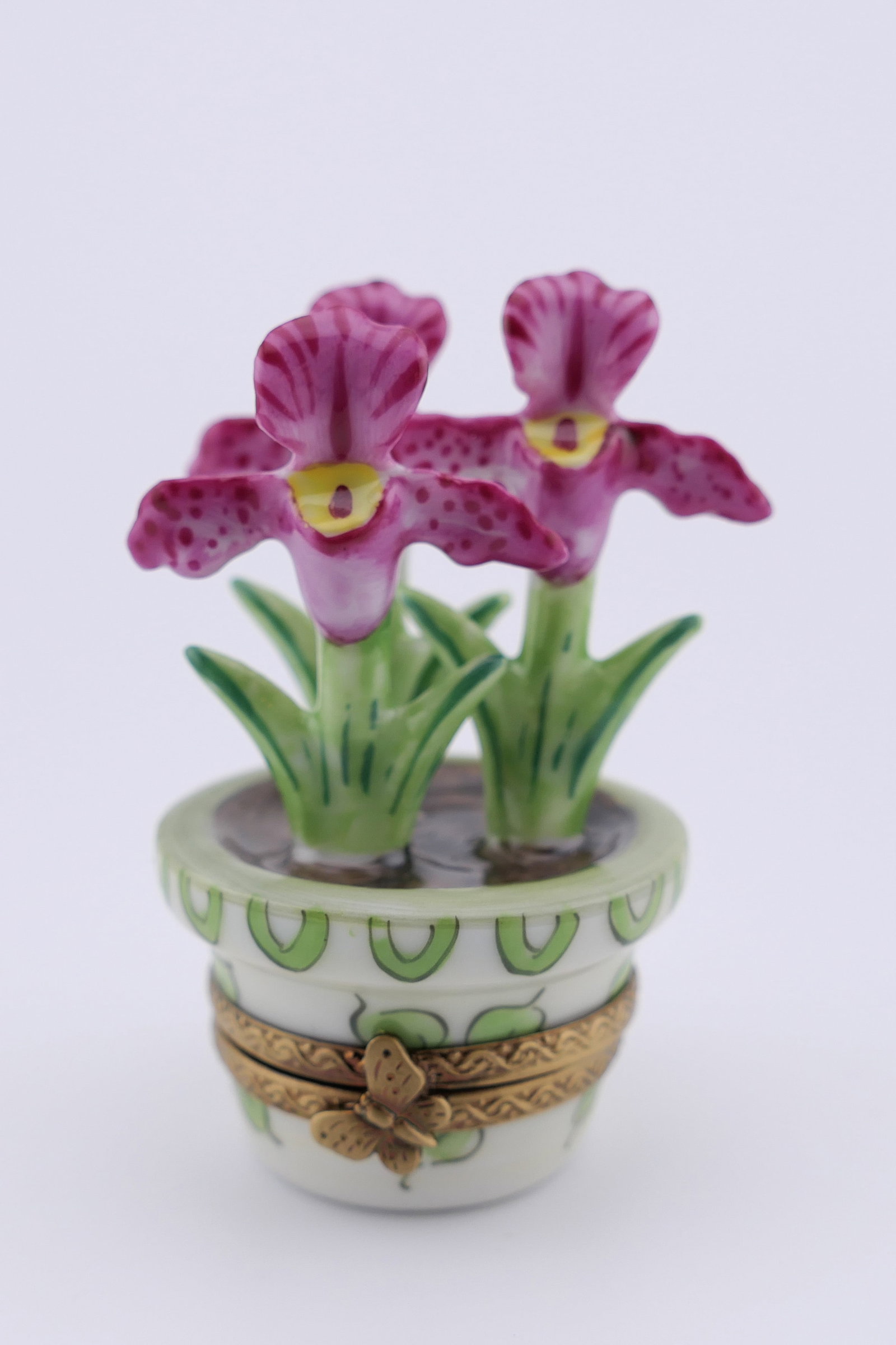Limoges Porcelain Orchid Trinket Box: Marked Limoges hand painted porcelain hinged trinket box featuring a design of a potted orchid plant with pink blossoms. Marked on the bottom Limoges France. Excellent condition. Size: 2.5"h Location: