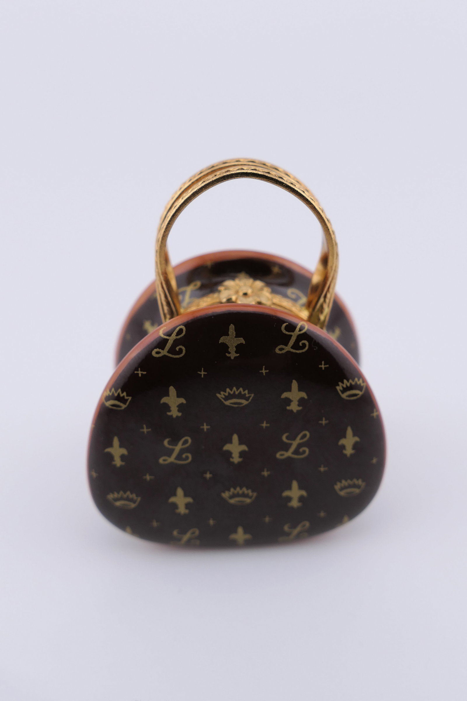 Limoges Porcelain Monogram Bag Trinket Box: Limoges hand painted porcelain hinged trinket box featuring a hand bag design in a style reminiscent of Louis Vuitton with a repeating monogram, and containing a miniature lipstick trinket. Marked ins