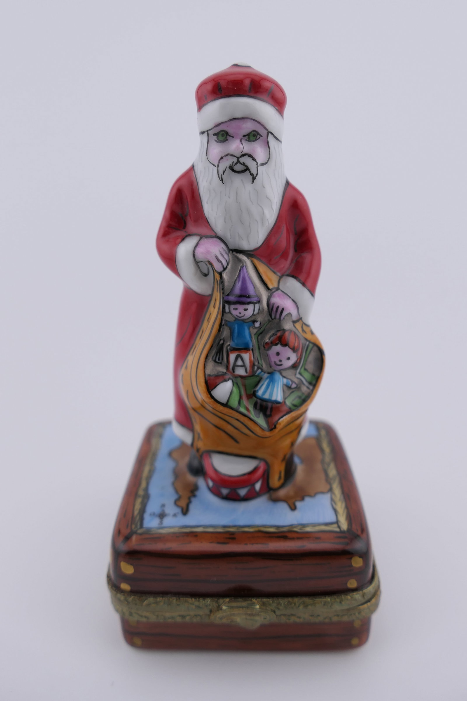 Limoges Porcelain Santa Trinket Box: Limoges hand painted porcelain hinged trinket box featuring a design of Santa Claus holding a sack of gifts. Marked on the bottom Limoges Frances. Excellent condition. Size: 3.75"h Location: Living Ro