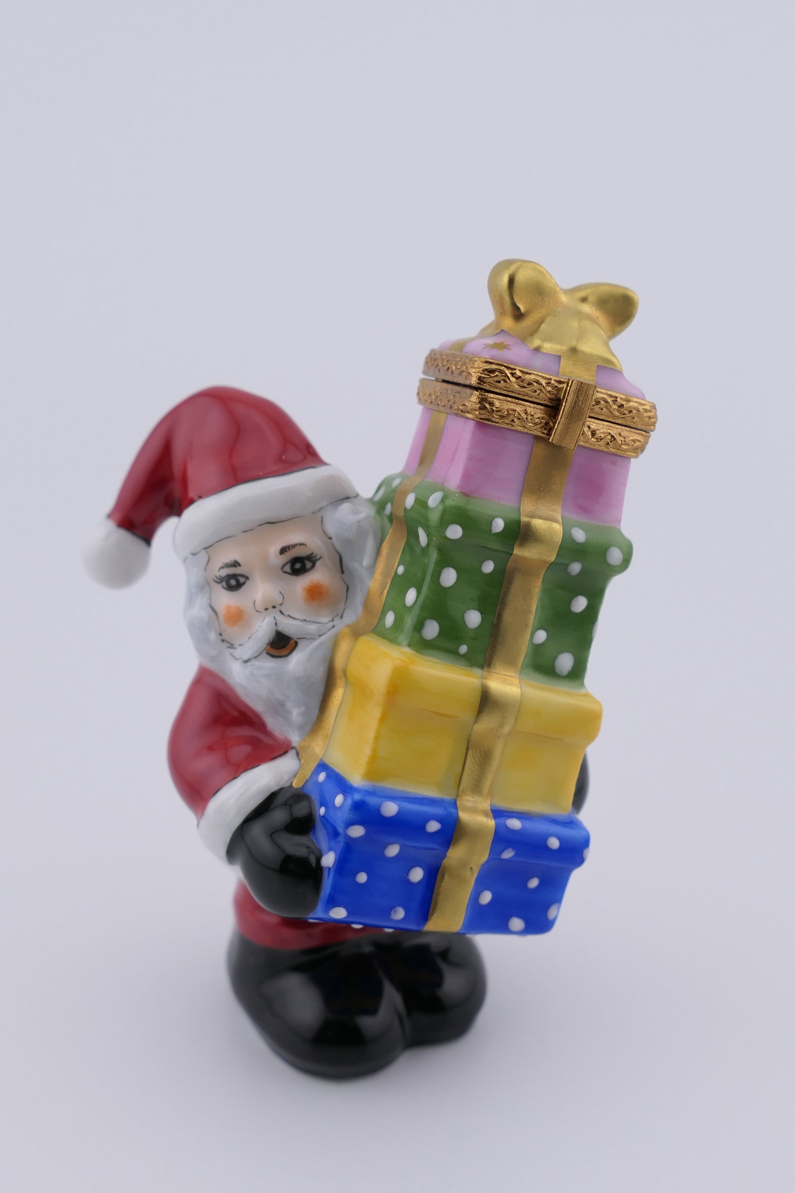 Limoges Porcelain Gifting Santa Trinket Box: Limoges hand painted porcelain hinged trinket box featuring a design of Santa Claus holding a stack of colorful gifts. Marked on the bottom Rochard Limoges France. Kept in original green velvet Rochar