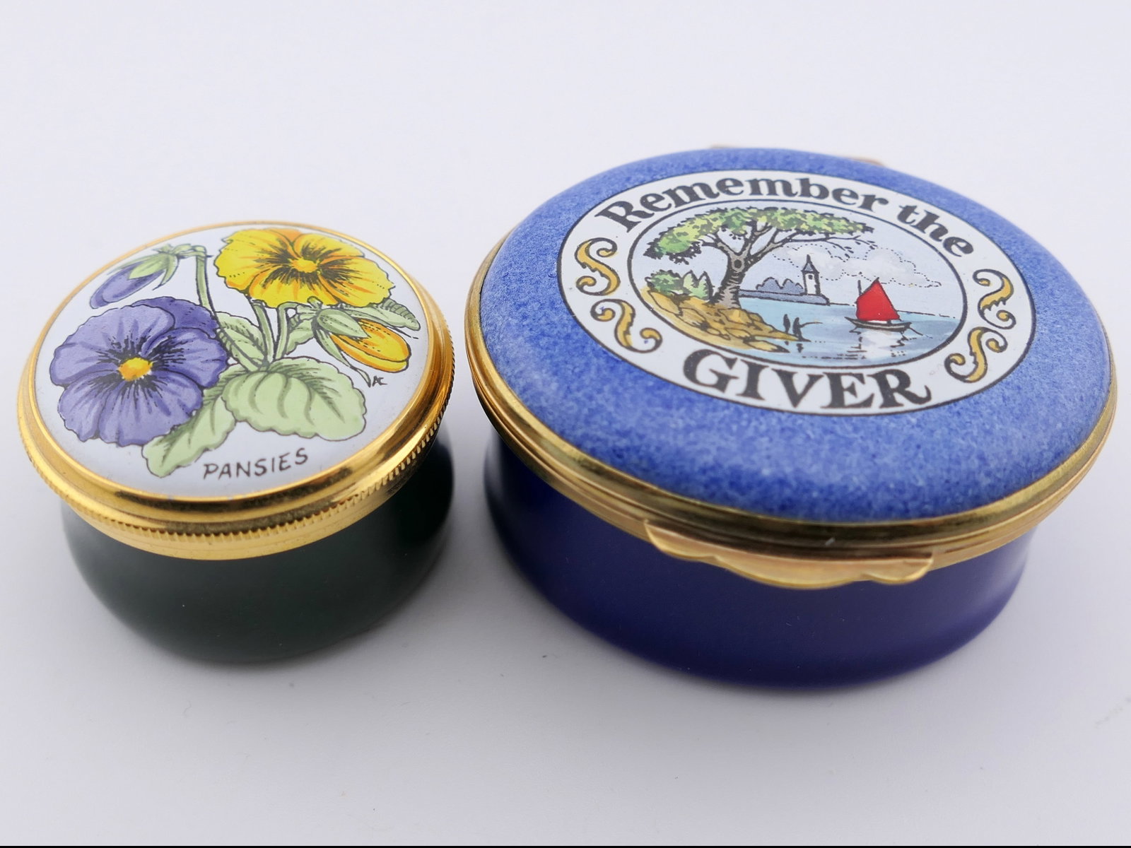 Two Crummels and Co Trinket Boxes: Two marked Crummels & Co trinket boxes with hinged and twist lids, featuring pansy and "Remember the Giver" motifs on the lids. Both are marked on the bottom Hand Painted in Fine Enamel, Made in Engla
